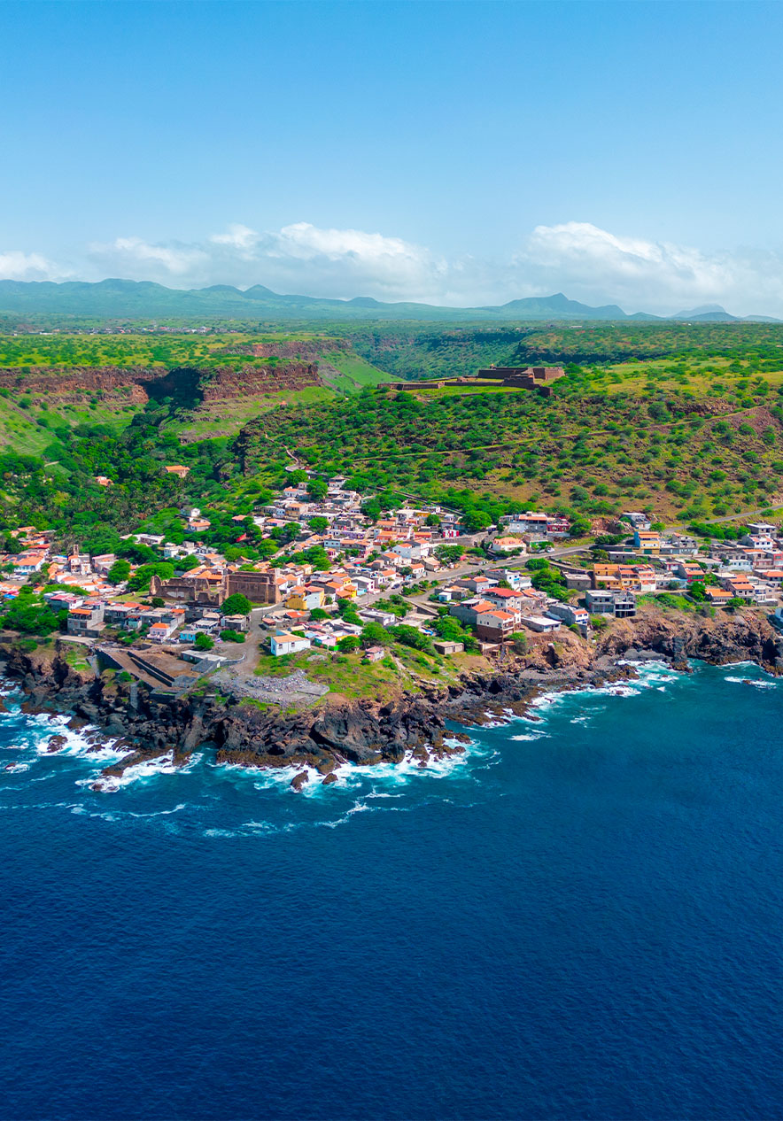 Vista de la Ciudad Vieja en la isla de Santiago, con mar azul, casas, vegetación y montañas al fondo