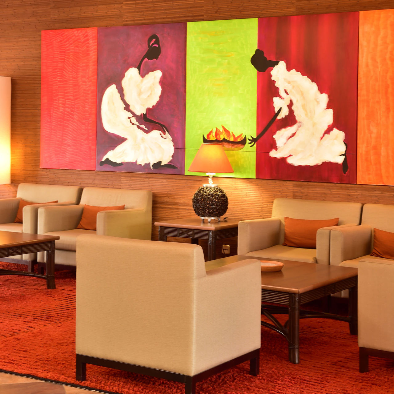 Lounge de recepción con tres sillones, mesa de noche con lámpara, y un cuadro pintado colgado en la pared