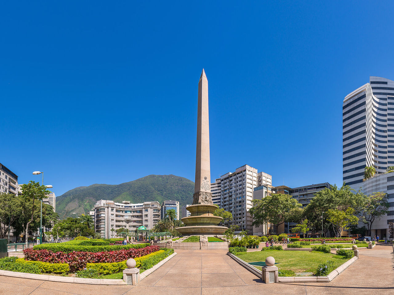 Monumento Obelisco, gran columna de piedra en medio de un parque con flores, rodeado de edificios altos en Caracas