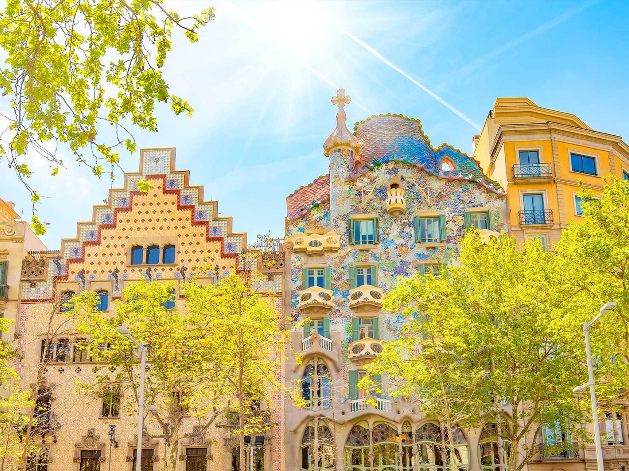 Icónico edificio de la Casa Batlló de Gaudí en Barcelona, con su colorida fachada, rodeado de árboles floridos