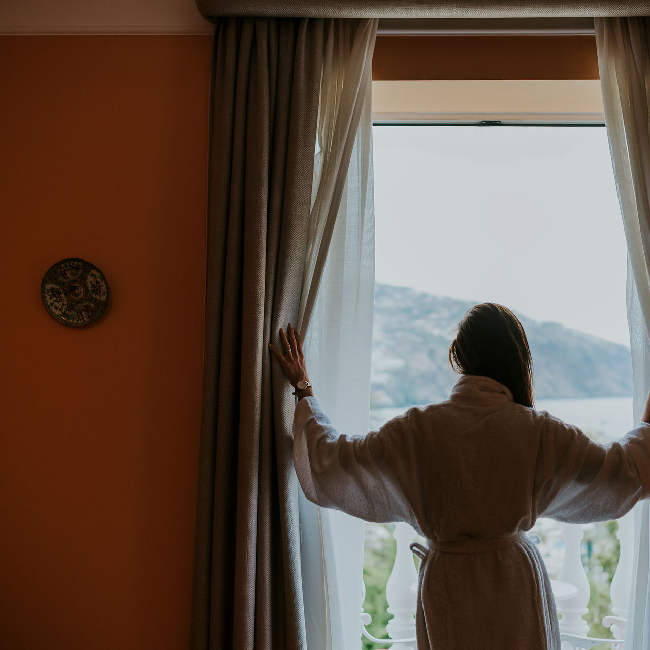 Señora en albornoz disfrutando de la vista al mar desde la ventana del Hotel en Madeira cerca de la playa, con piscina