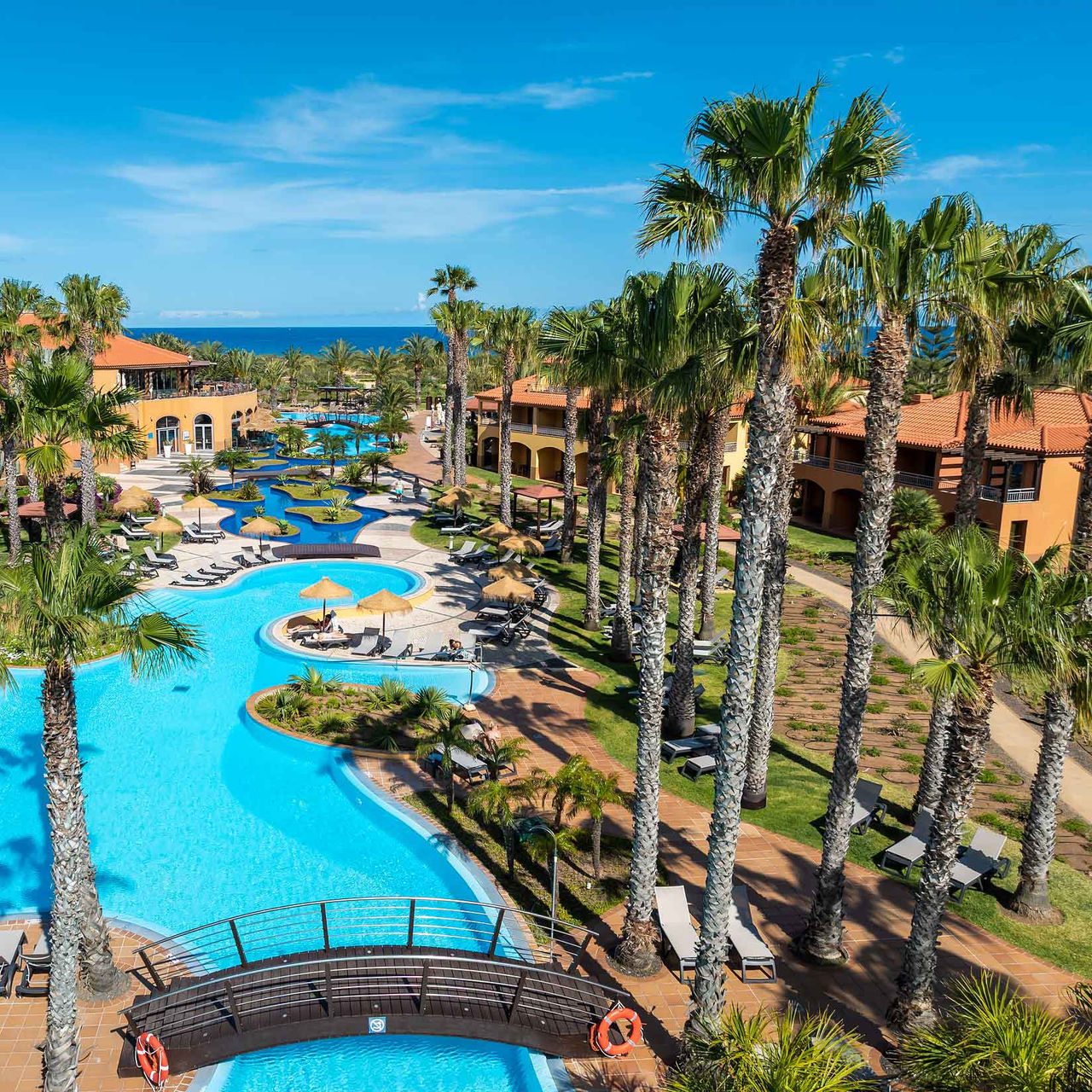 Piscina del resort de 5 estrellas en Porto Santo, rodeada de palmeras tropicales, tumbonas y jardín.