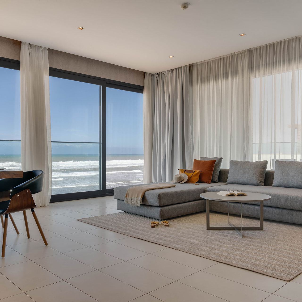 Sala com vista mar, um sofá confortável e acolhedor com chaise lounge e uma mesa com cadeiras de design moderno