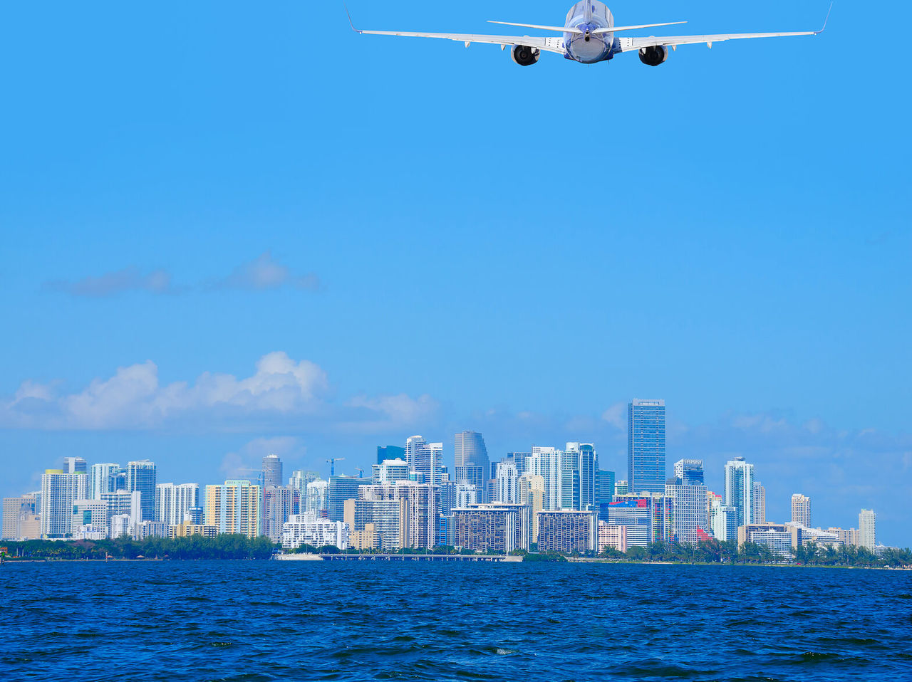 Avião a levantar voo sobre a cidade Miami, com prédios altos e céu azul 