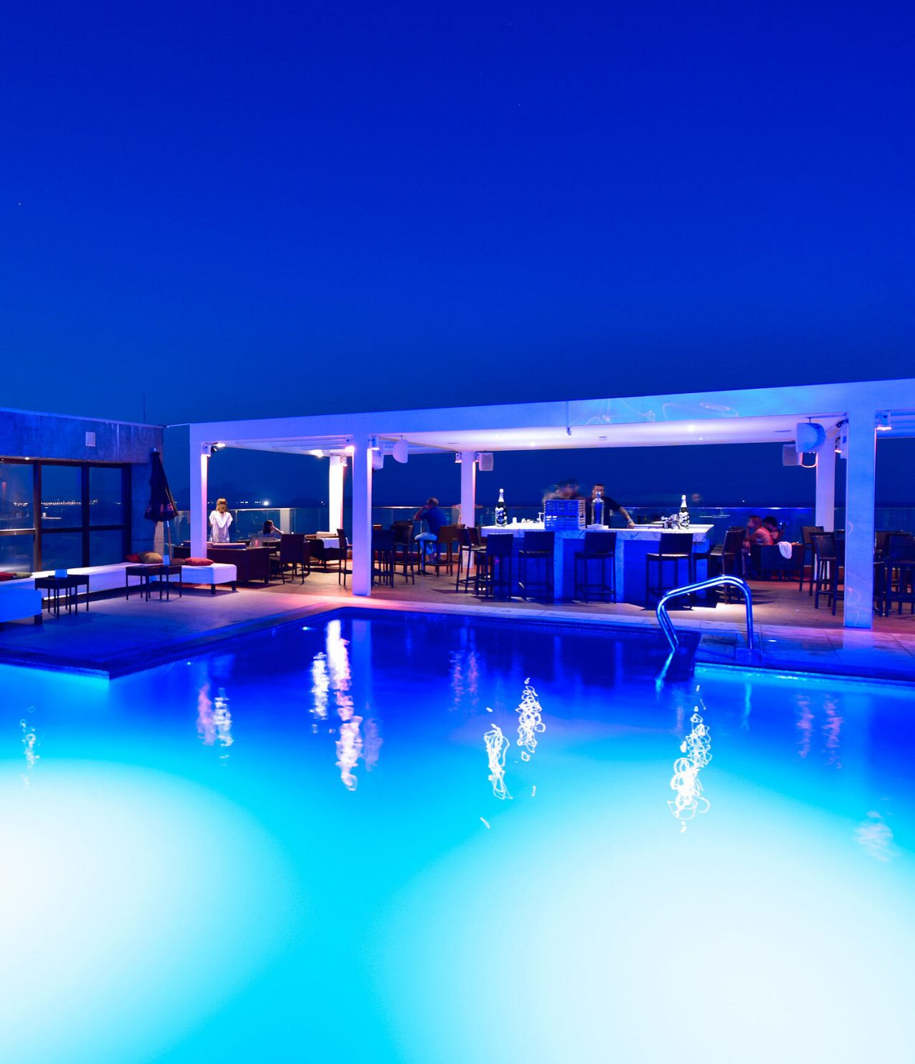 O bar Deck, do Hotel 4 Estrelas no Rio de Janeiro, tem um bar em cima da piscina, com mesas, que serve bebidas como cocktails