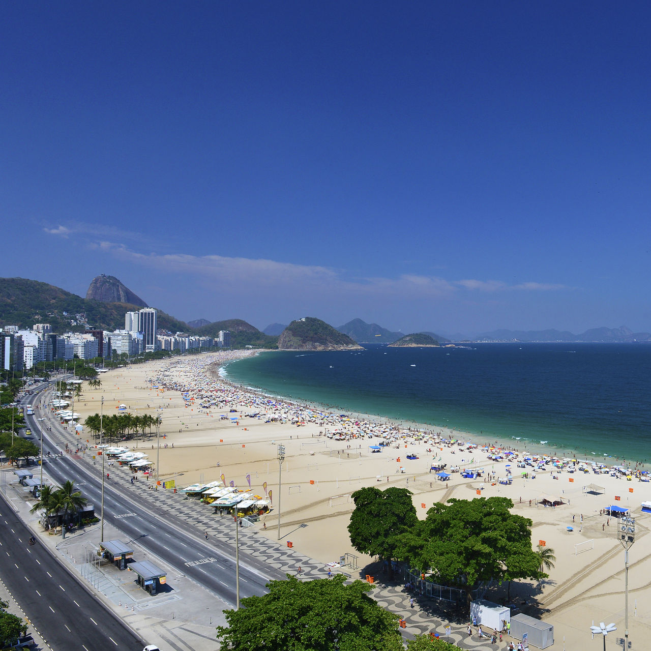 Praia de Copacabana no Rio de Janeiro, praia movimentada com areia dourada, mar azul e montanhas ao fundo