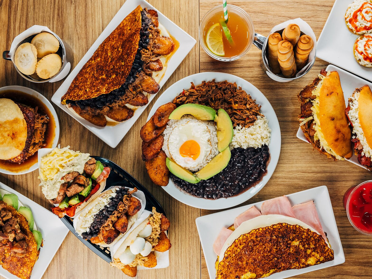 Mesa repleta de pratos típicos da gastronomia venezuelana, incluindo arepas, tequeños e chapachas