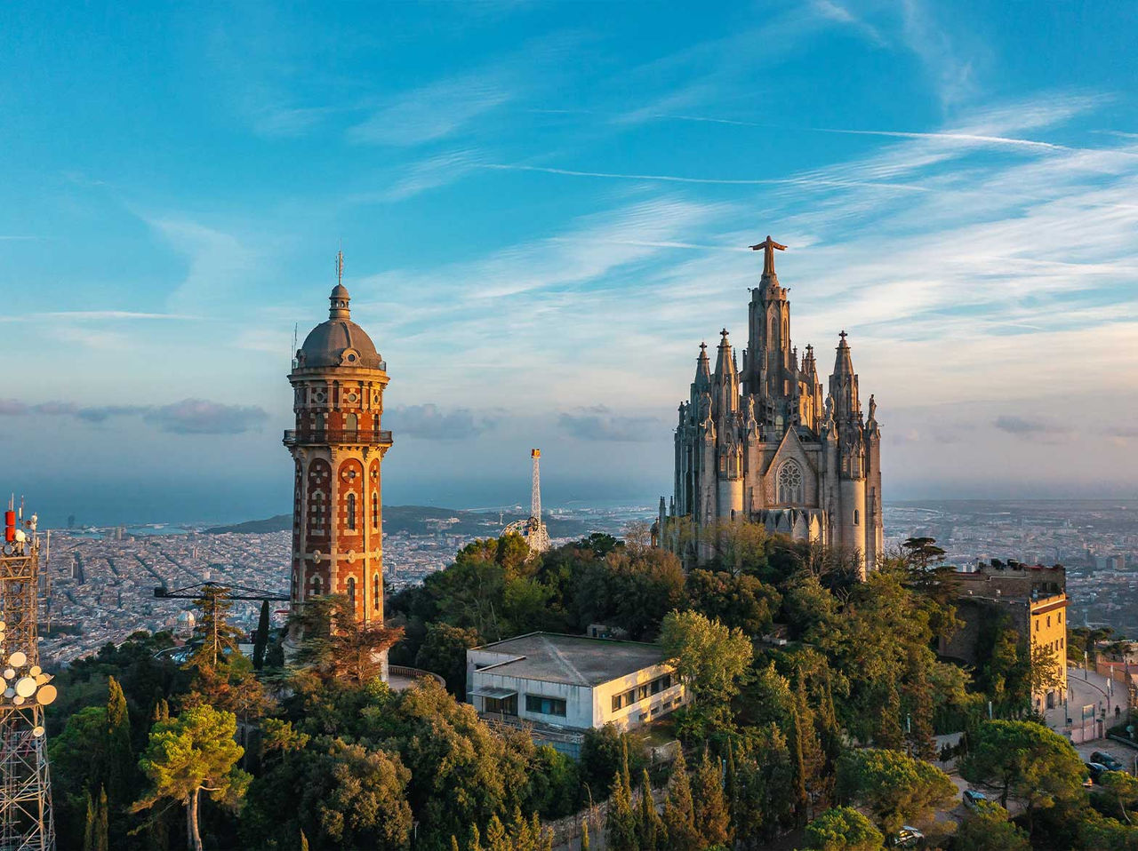 Vista do icónico templo Sagrado Coração de Jesus no Tibidabo, cercado por vegetação e com a cidade de Barcelona no fundo