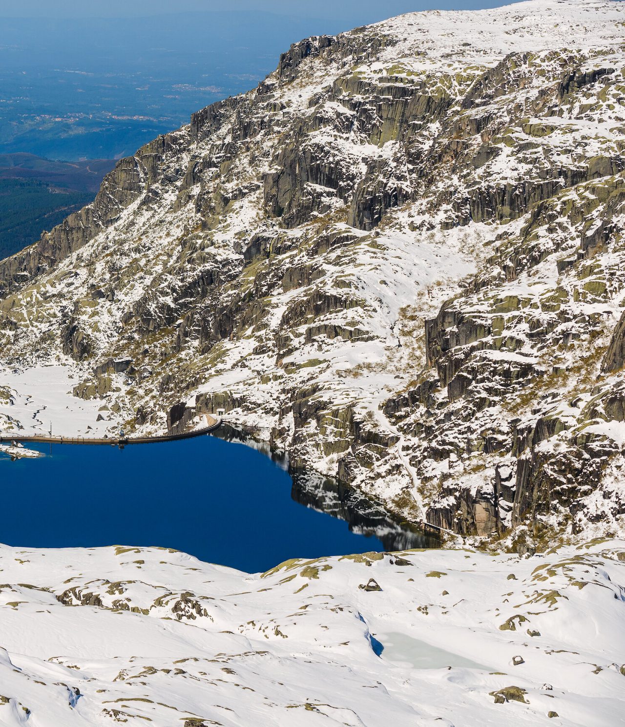 A beleza intocada da natureza montanhosa, contrastando o lago azul-turquesa com a brancura da neve