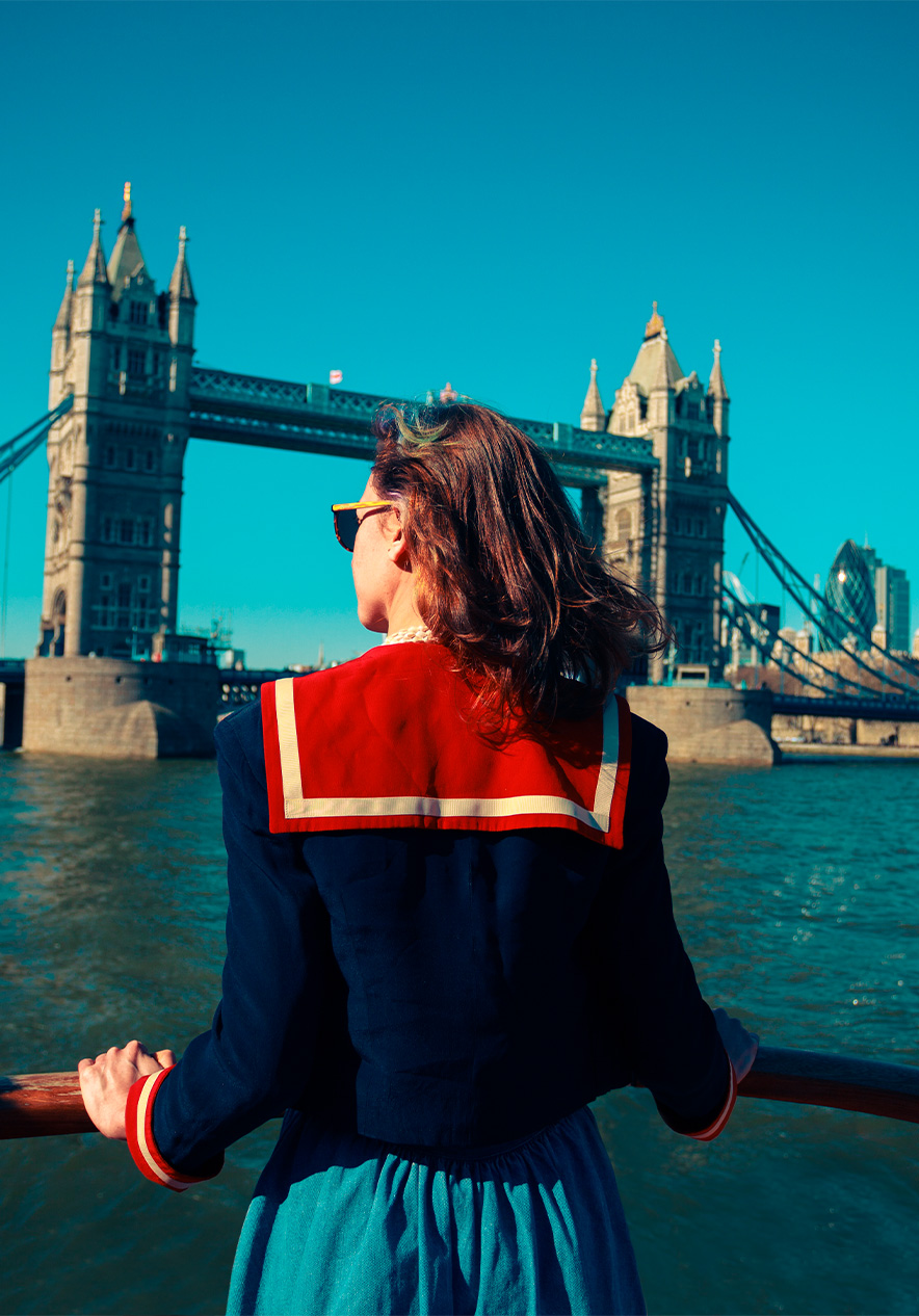 Passeio de barco no Rio Tamisa com uma senhora na frente do barco, virada para Tower Bridge, com o céu limpo