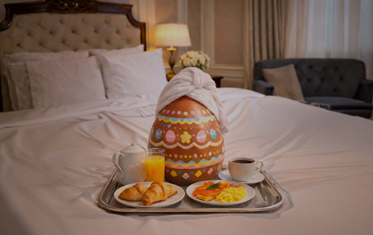 Ovo da Páscoa decorado com toalha na cama, pequeno-almoço com croissants, café e sumo de laranja