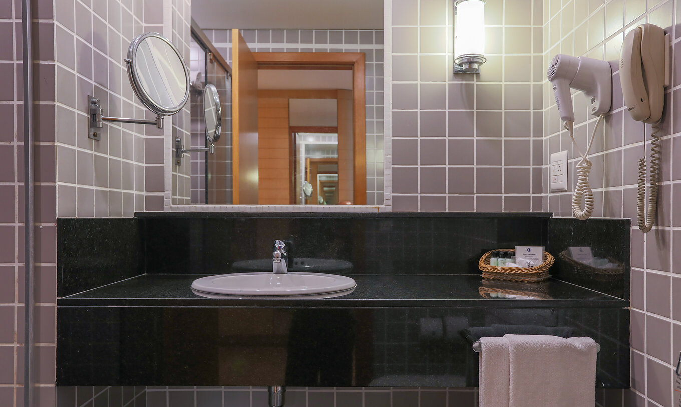 The Deluxe Corner at Pestana Curitiba has a bathroom with gray tiles and a black countertop with a sink