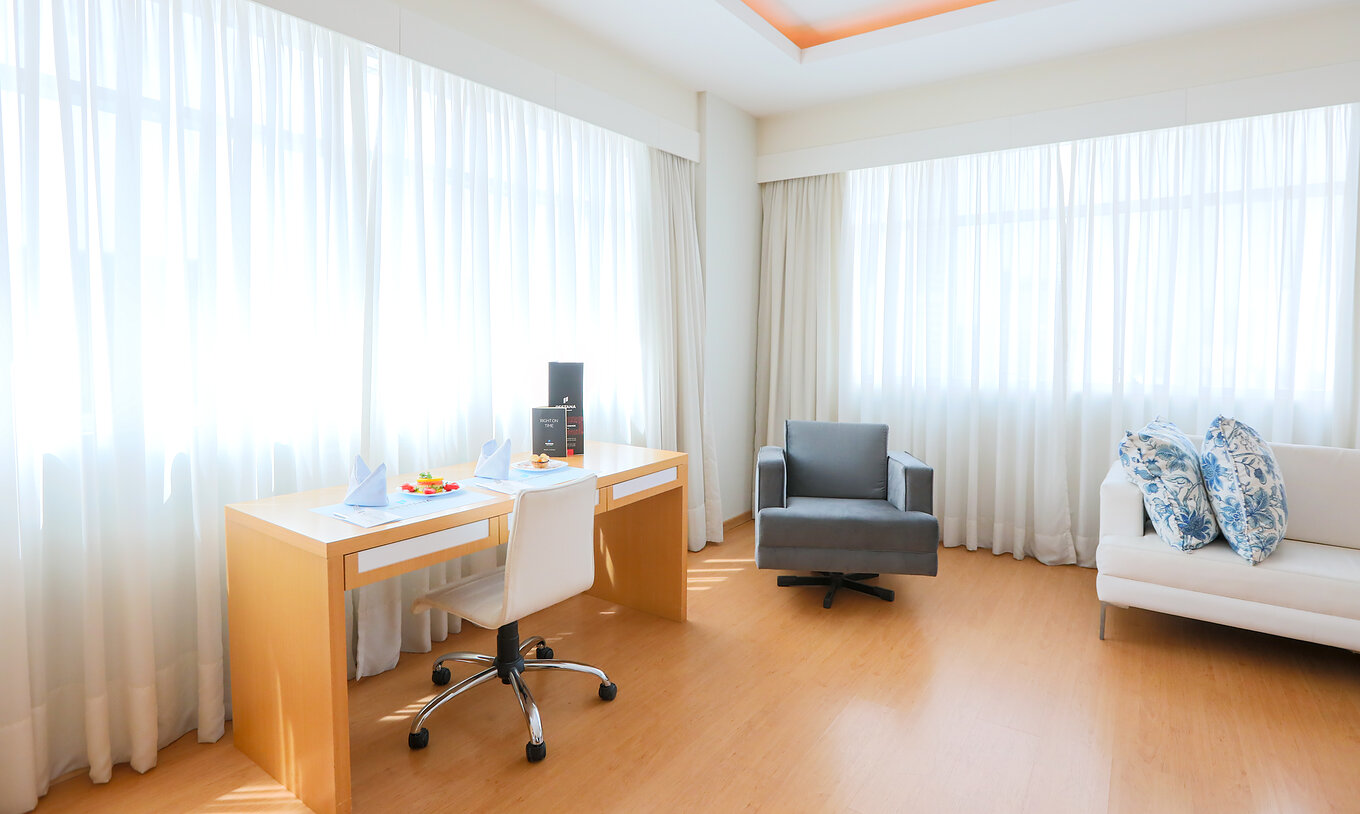 The Deluxe Corner at Pestana Curitiba has sofas and a desk next to two large windows that let in plenty of light