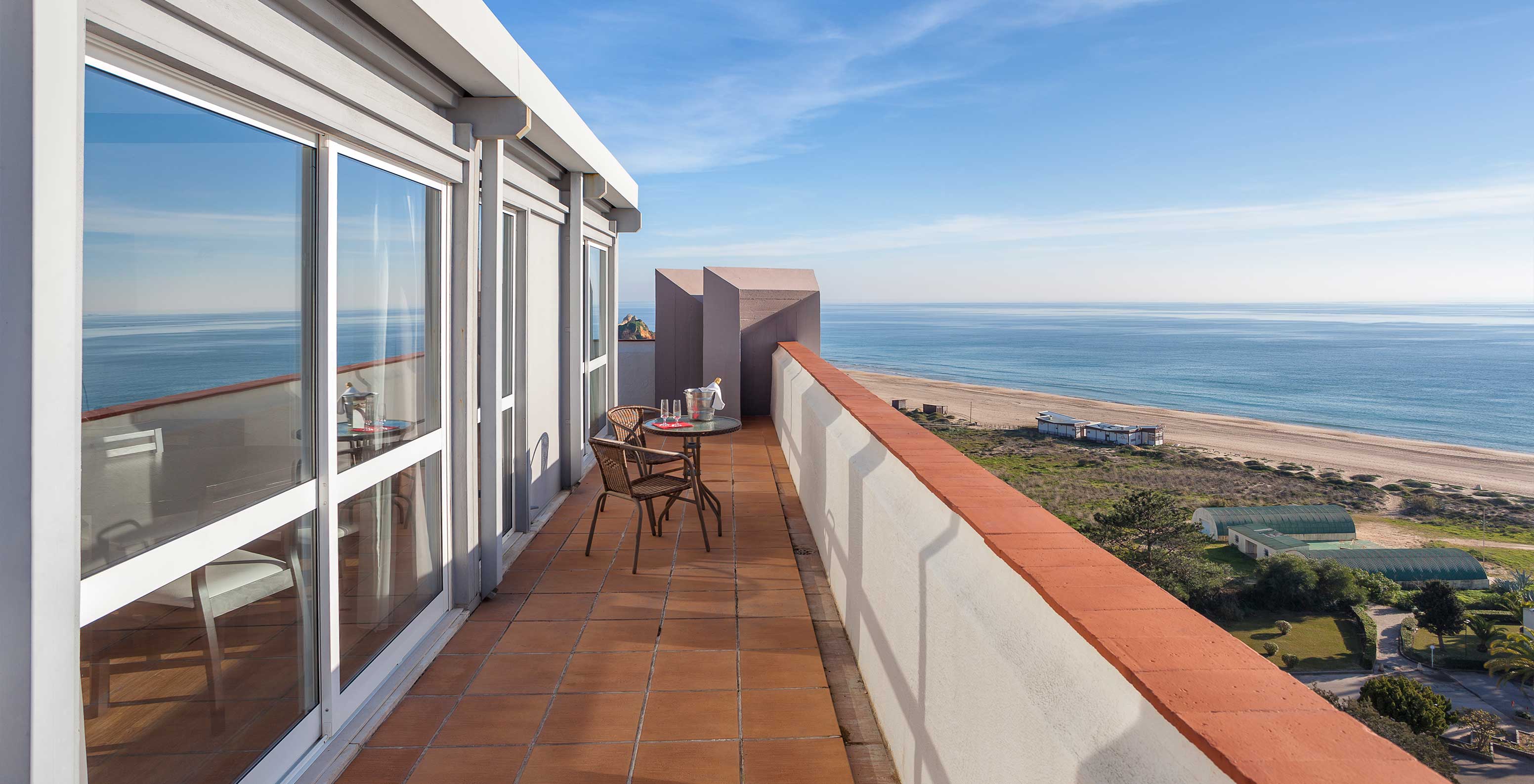 The T1 Sea View Apartment at Pestana Alvor Atlântico has a balcony with a table and two chairs, overlooking the beach and sea