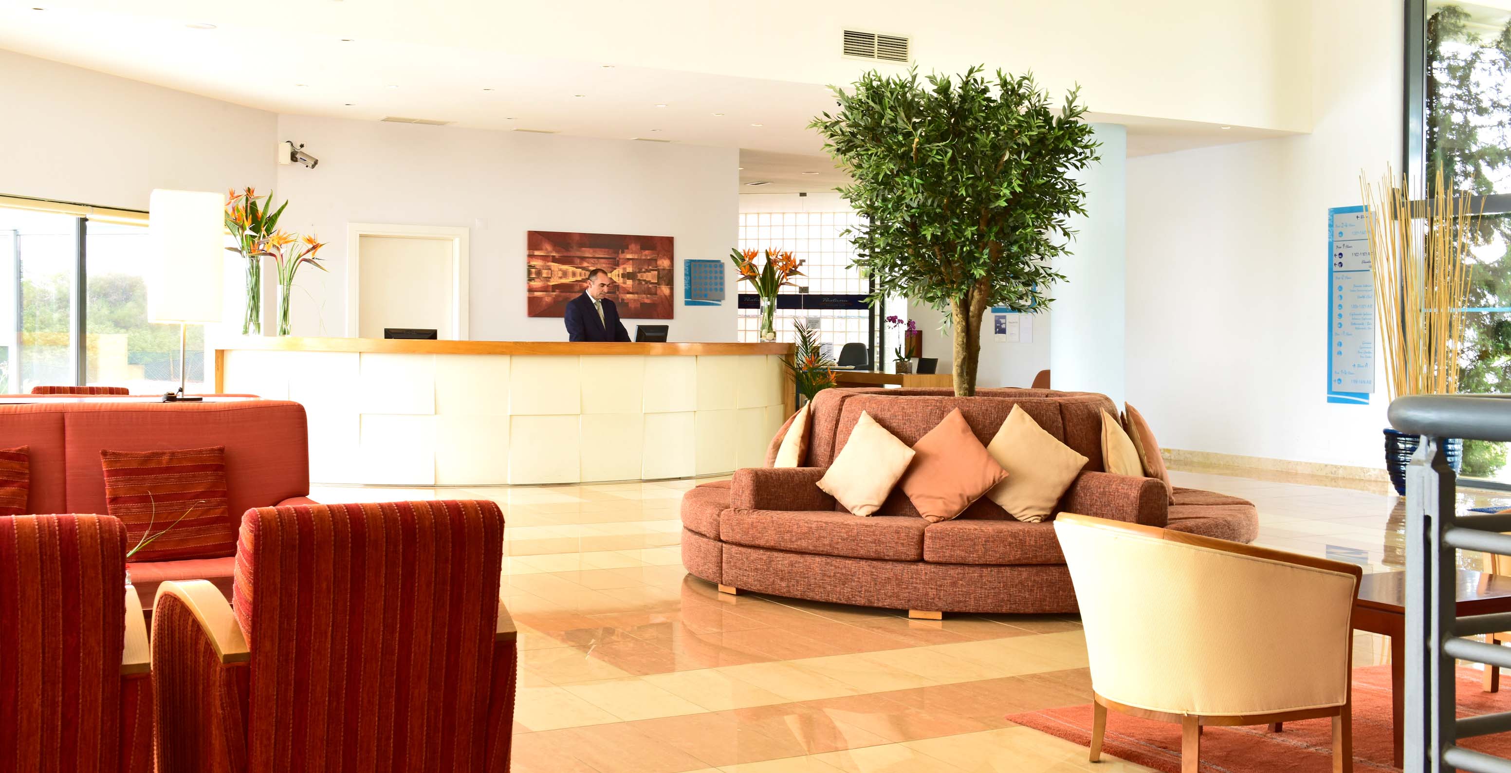 Reception of the Pestana Alvor Park hotel with red sofas and armchairs with flowers in vases and a tree in the center