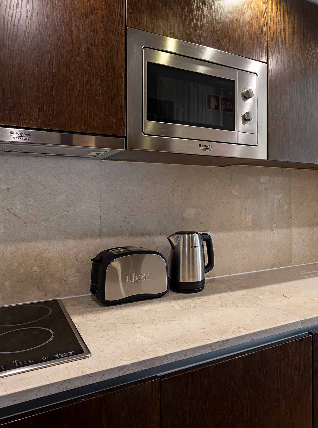 The Cliff Studio at Pestana Alvor Praia has a dark wood kitchen and a stone countertop, with a stove and a microwave