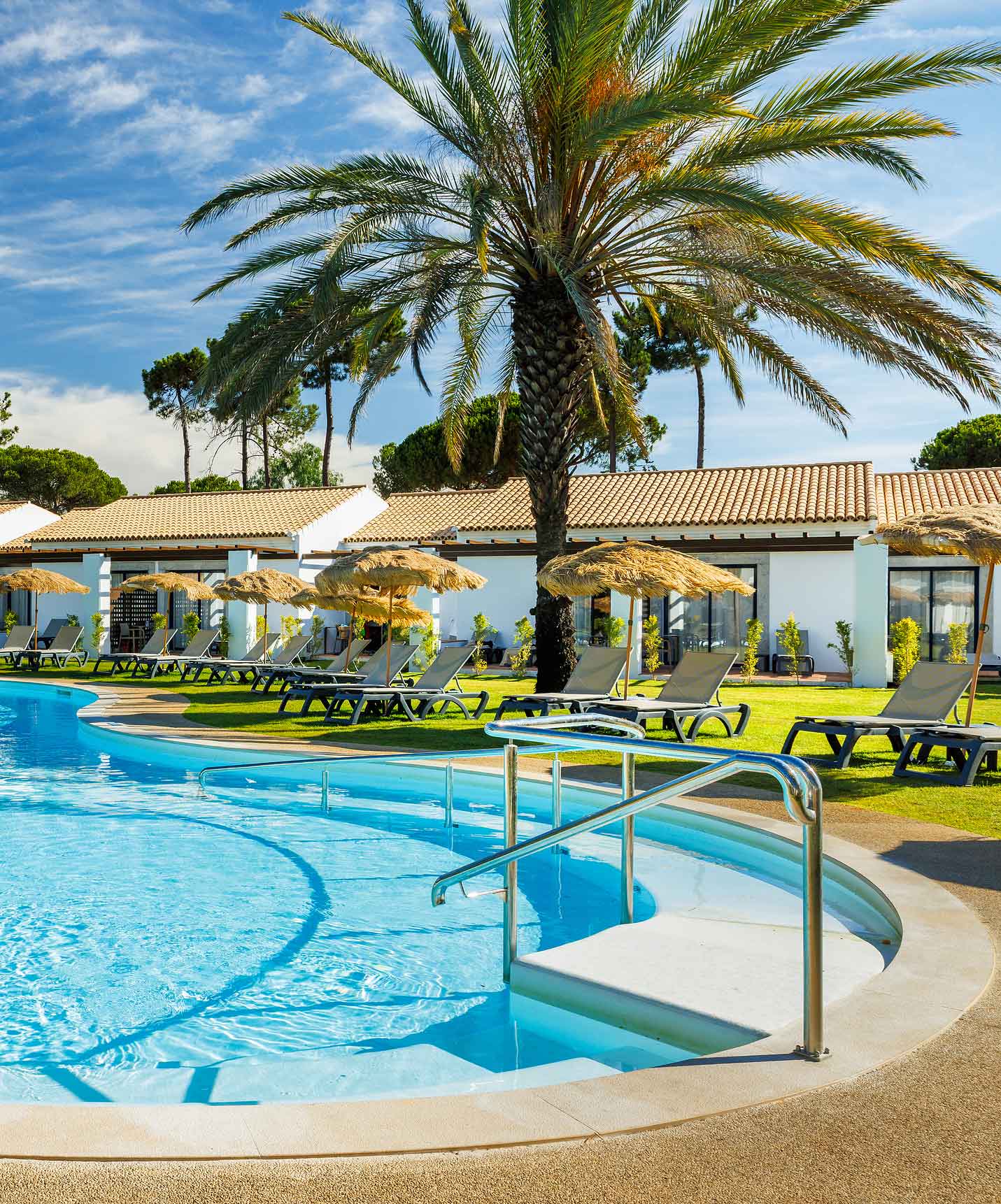 Outdoor pool with sun loungers, surrounded by vegetation and palm trees at the Hotel with Golf and Spa in the Algarve