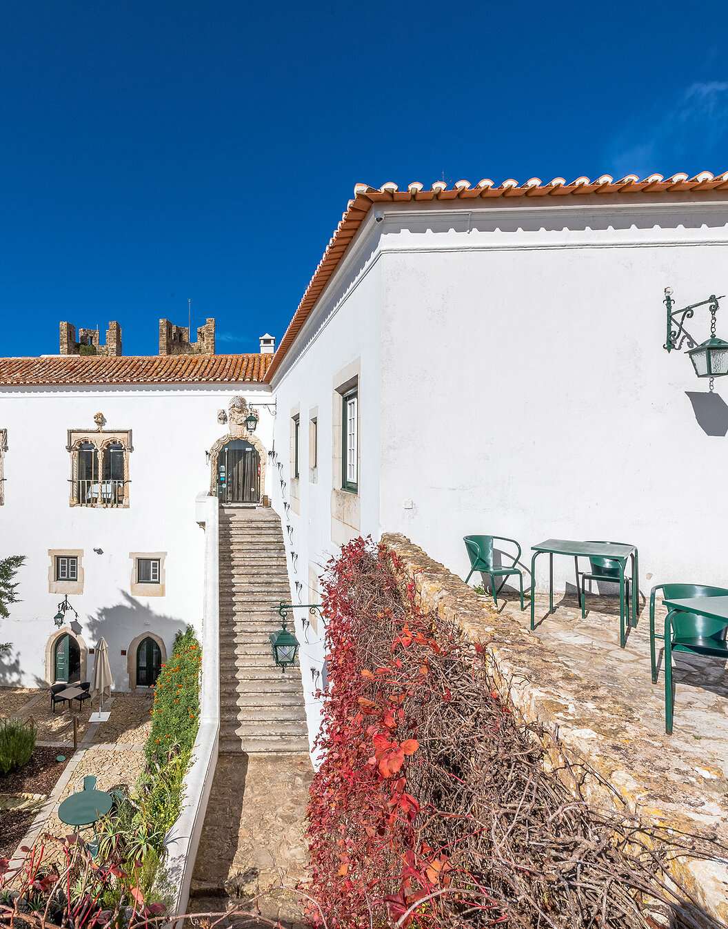 Exterior view of the façade of Pousada Castelo Óbidos, with its gardens, chairs, and tables around
