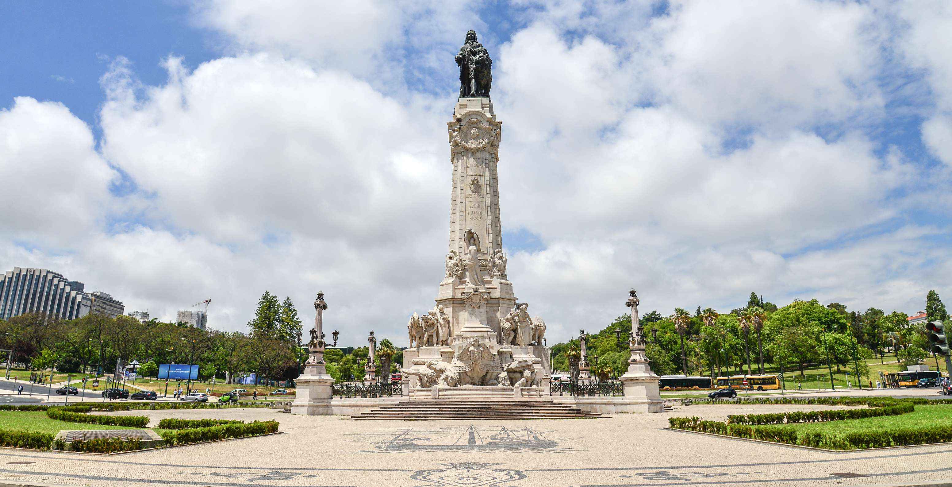 View from below of the Marquês de Pombal statue, surrounded by flower beds, trees, and a cloudy sky