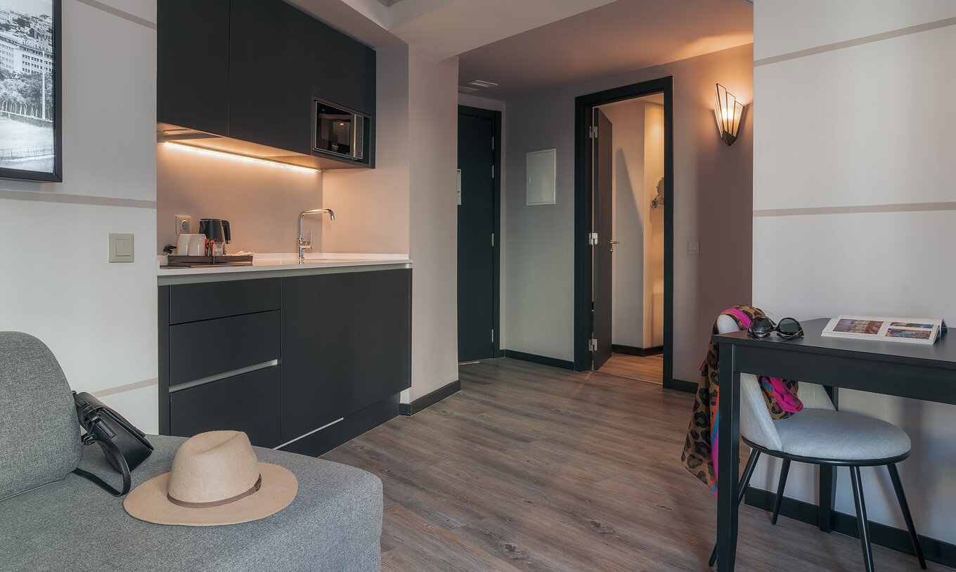 The Double Deluxe Studio at Pestana Lisboa Vintage has a kitchenette with microwave, a table with chair and a gray sofa