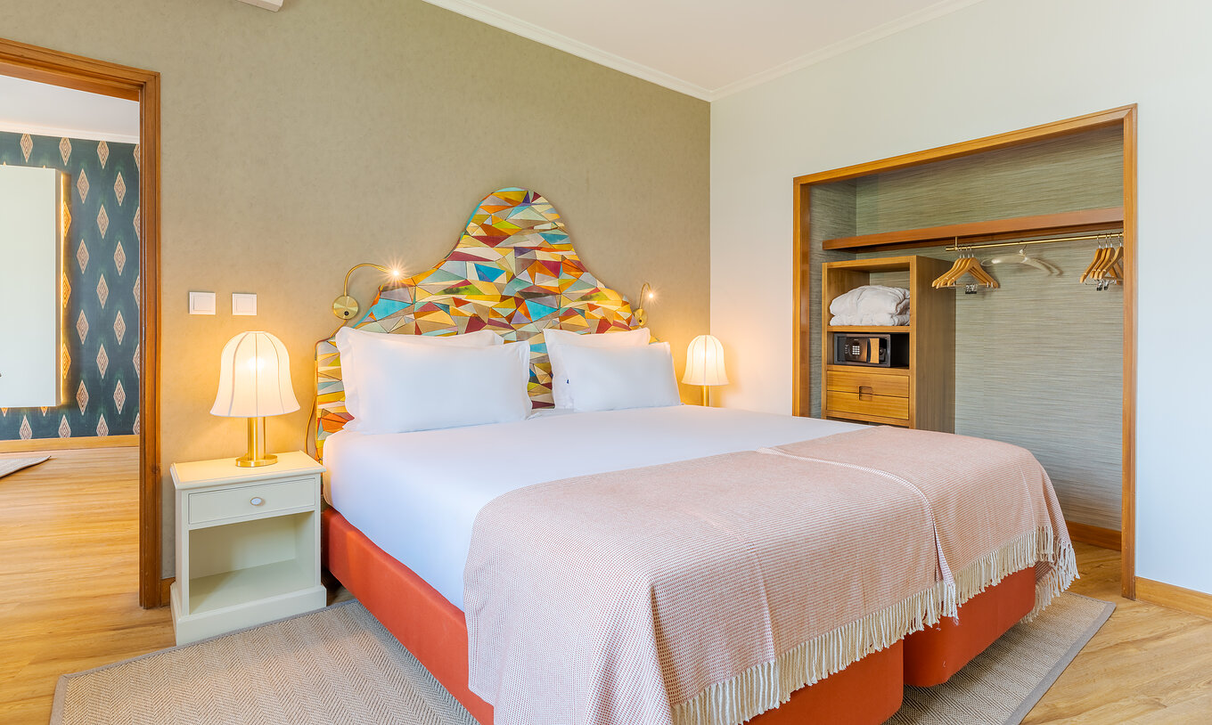 The Superior Lateral Sea View Suite at Pestana Vila Lido Madeira features a double bed with a colorful headboard and wardrobe