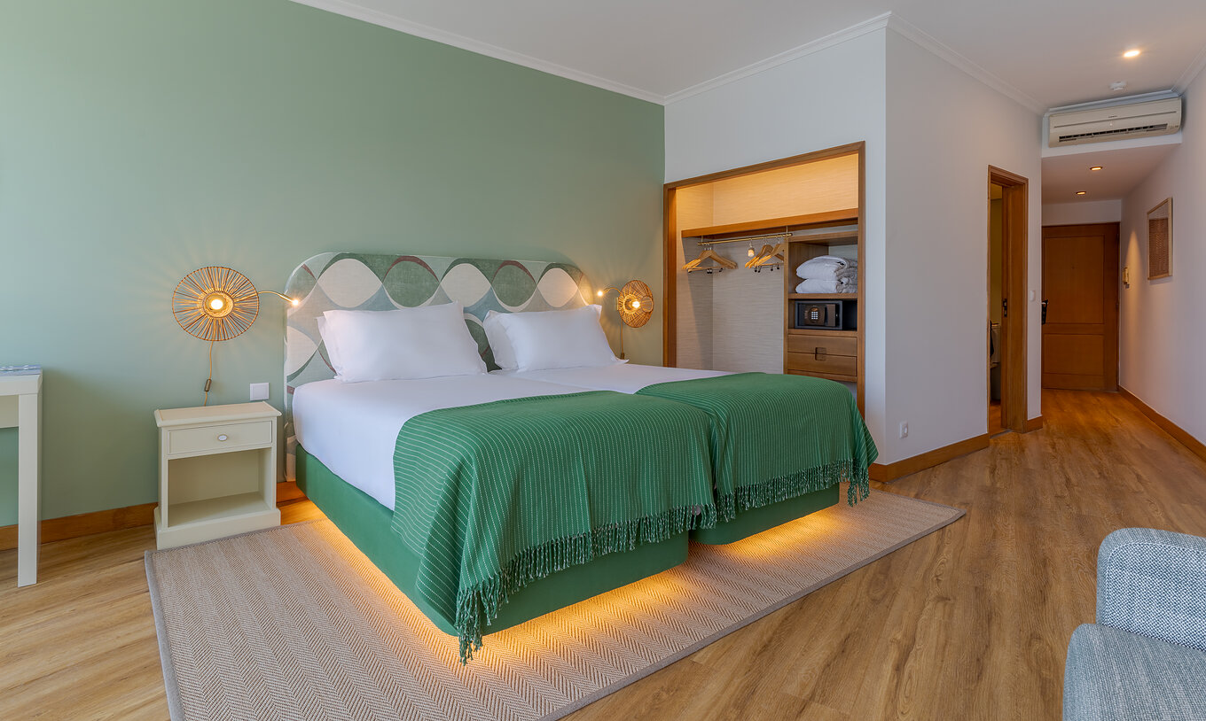 The Superior Sea View room at Pestana Vila Lido Madeira features green tones, two beds, and a wardrobe with safe