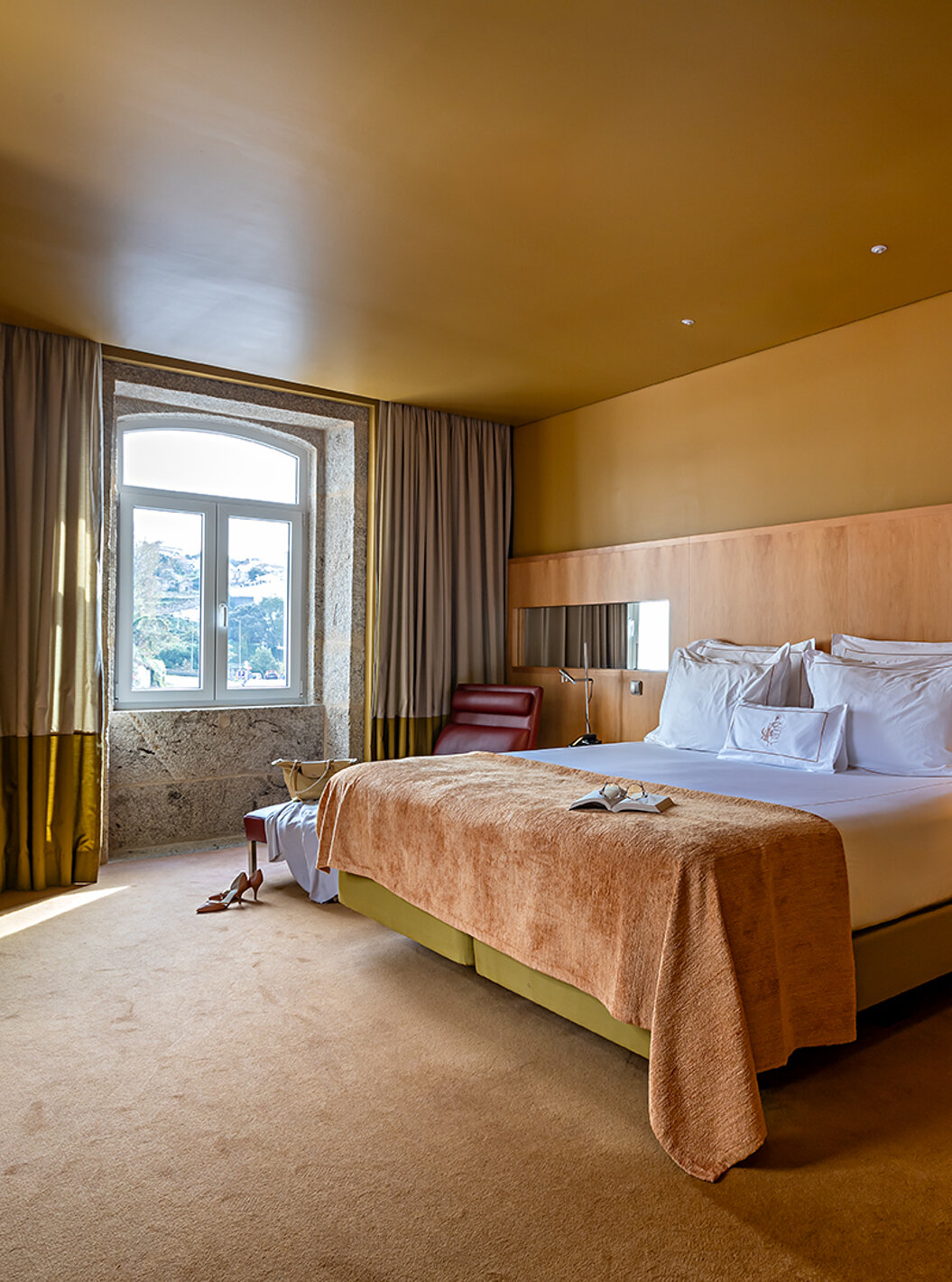 The Junior Suite has a double bed with a beige blanket and a stone-framed window with river view
