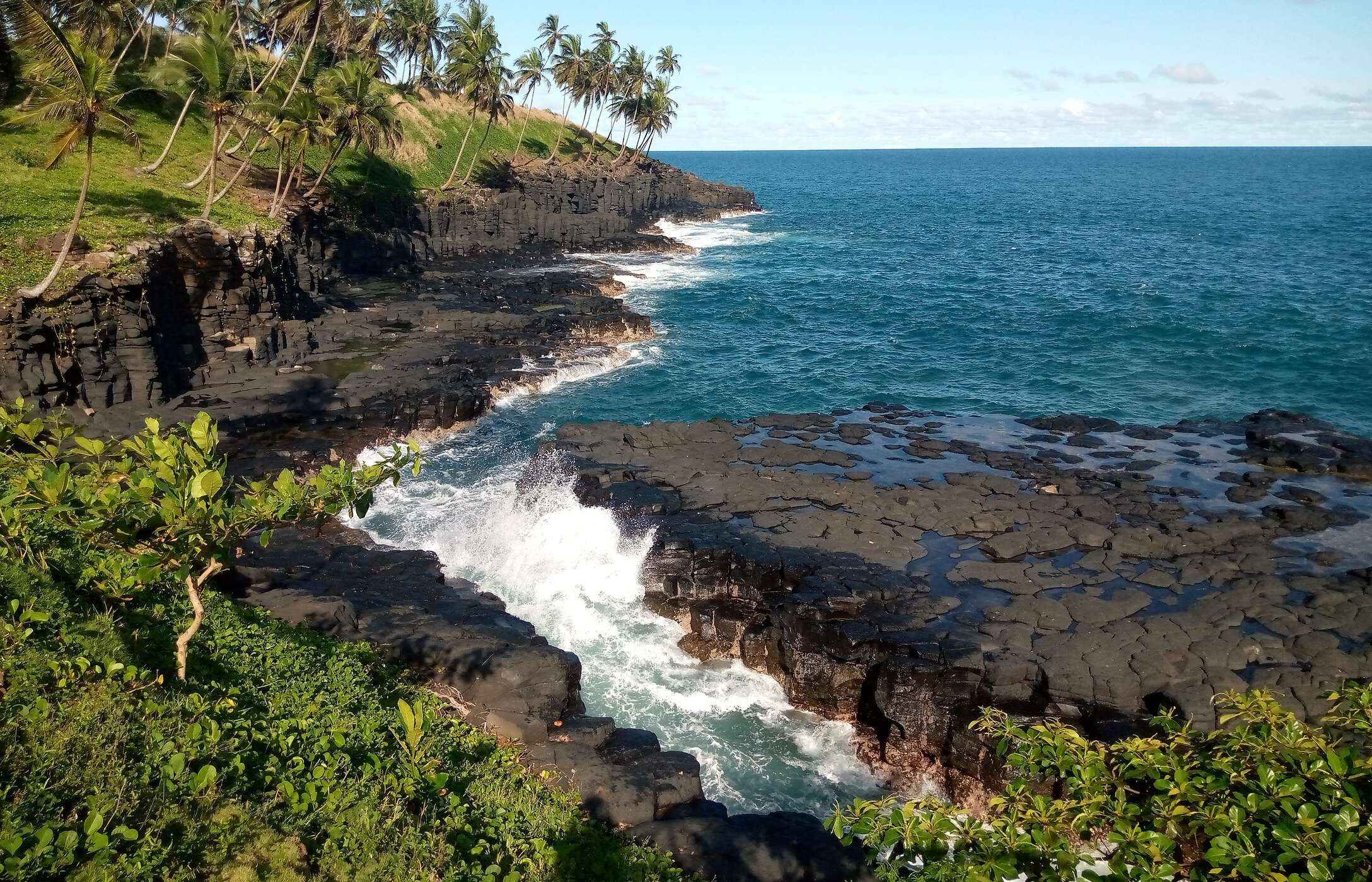 View of Hell's Mouth in São Tomé and Príncipe, with rough seas, black rocks, and surrounding vegetation.