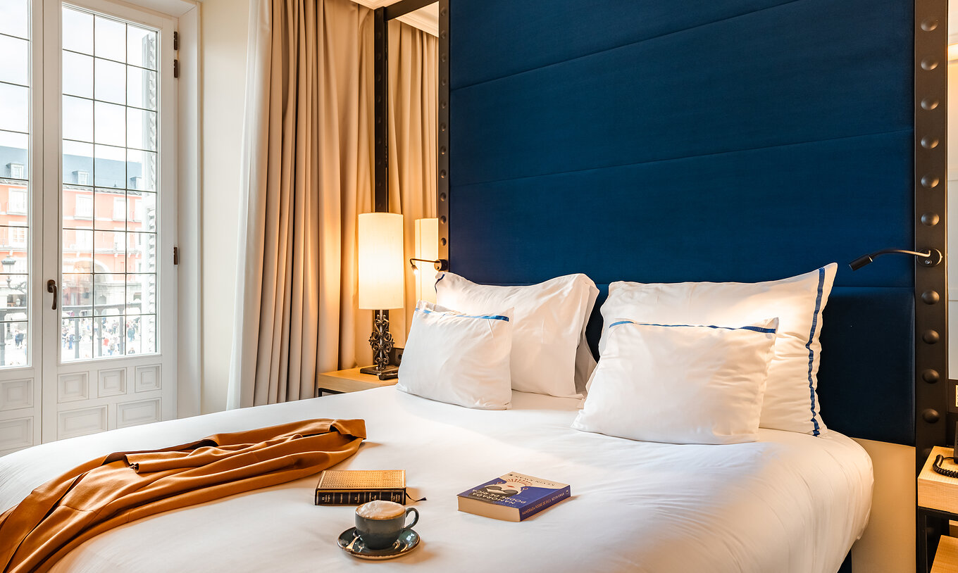 The Superior Plaza Mayor at Pestana Plaza Mayor Madrid has a double bed with blue headboard with mirror and a large window