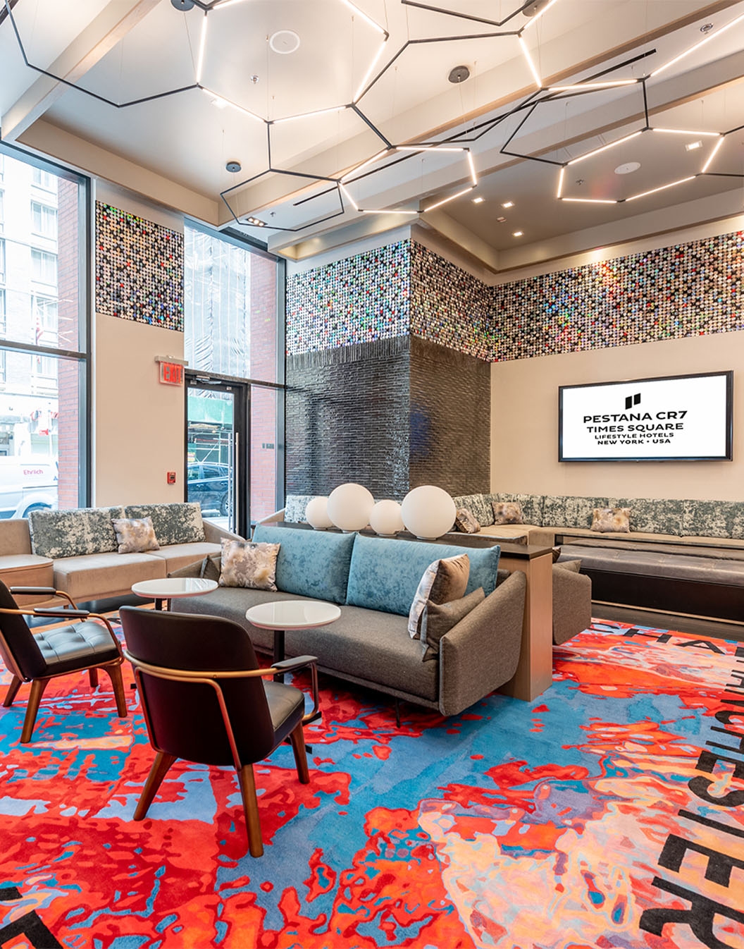 Interior view of the lobby of Pestana CR7 Times Square, with comfortable sofas, chairs, and a vibrant rug