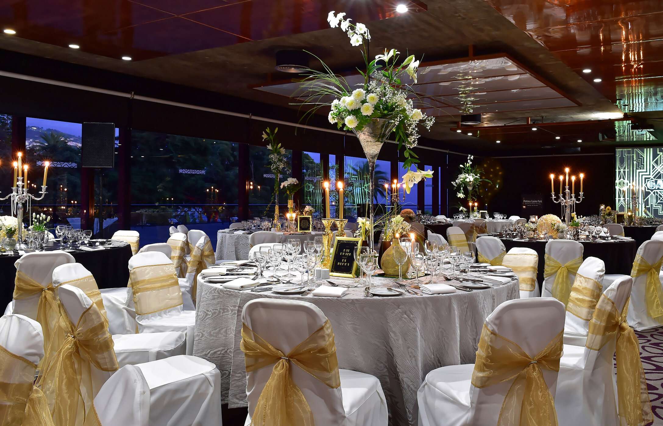 Wedding in a room with modern decor, round tables with tall floral arrangements, and soft, elegant lighting