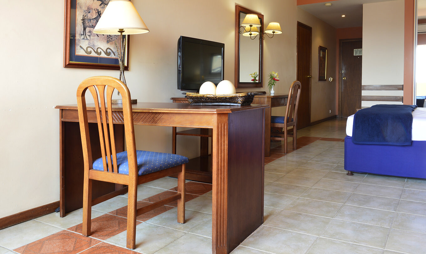 La Suite Executiva Familiar del Pestana Rovuma tiene un escritorio y una silla de madera, con una lámpara y un cuadro