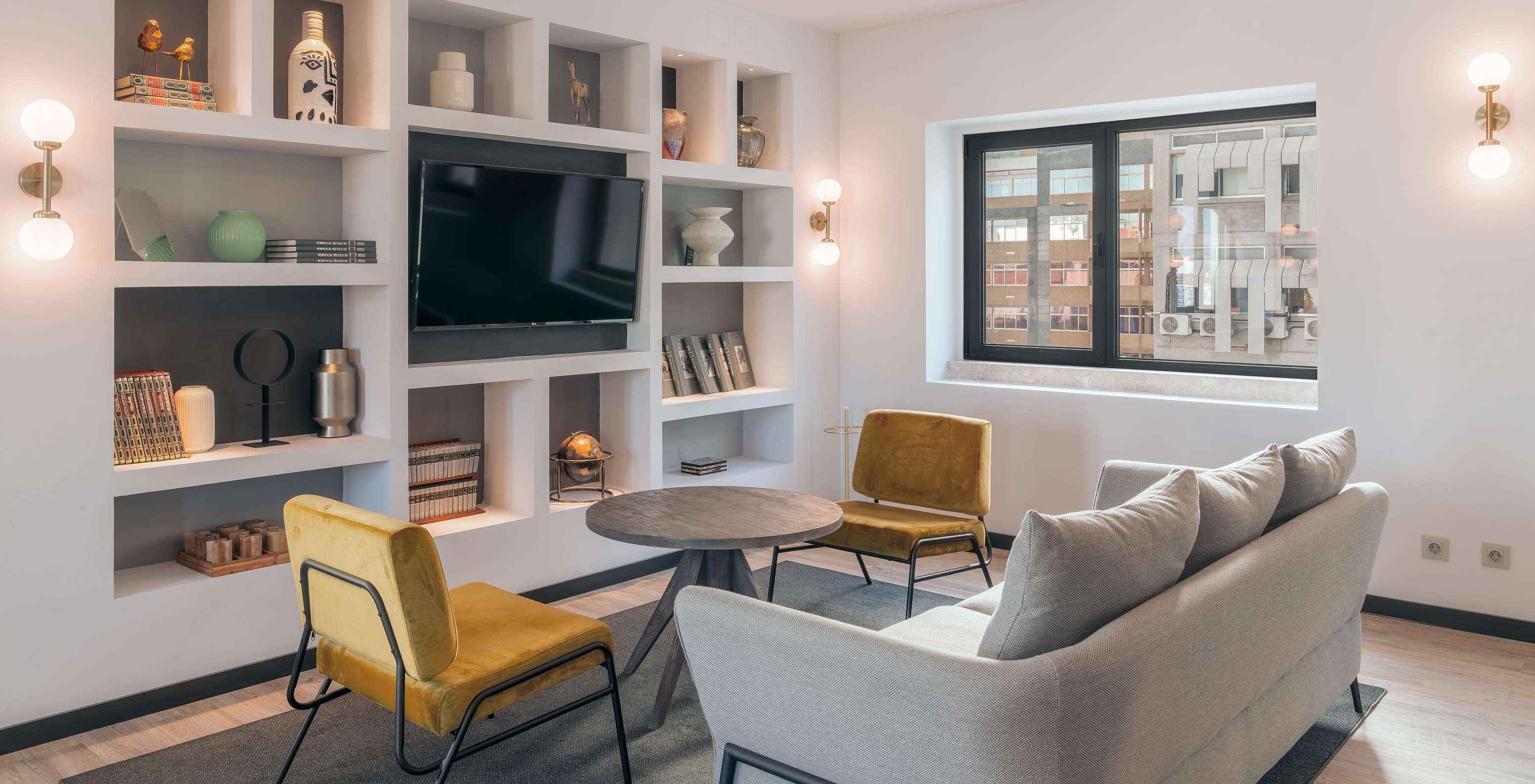 Lounge con sofá, sillas, mesa auxiliar, televisión, alfombra y objetos de decoración con ventanas con vista a la ciudad