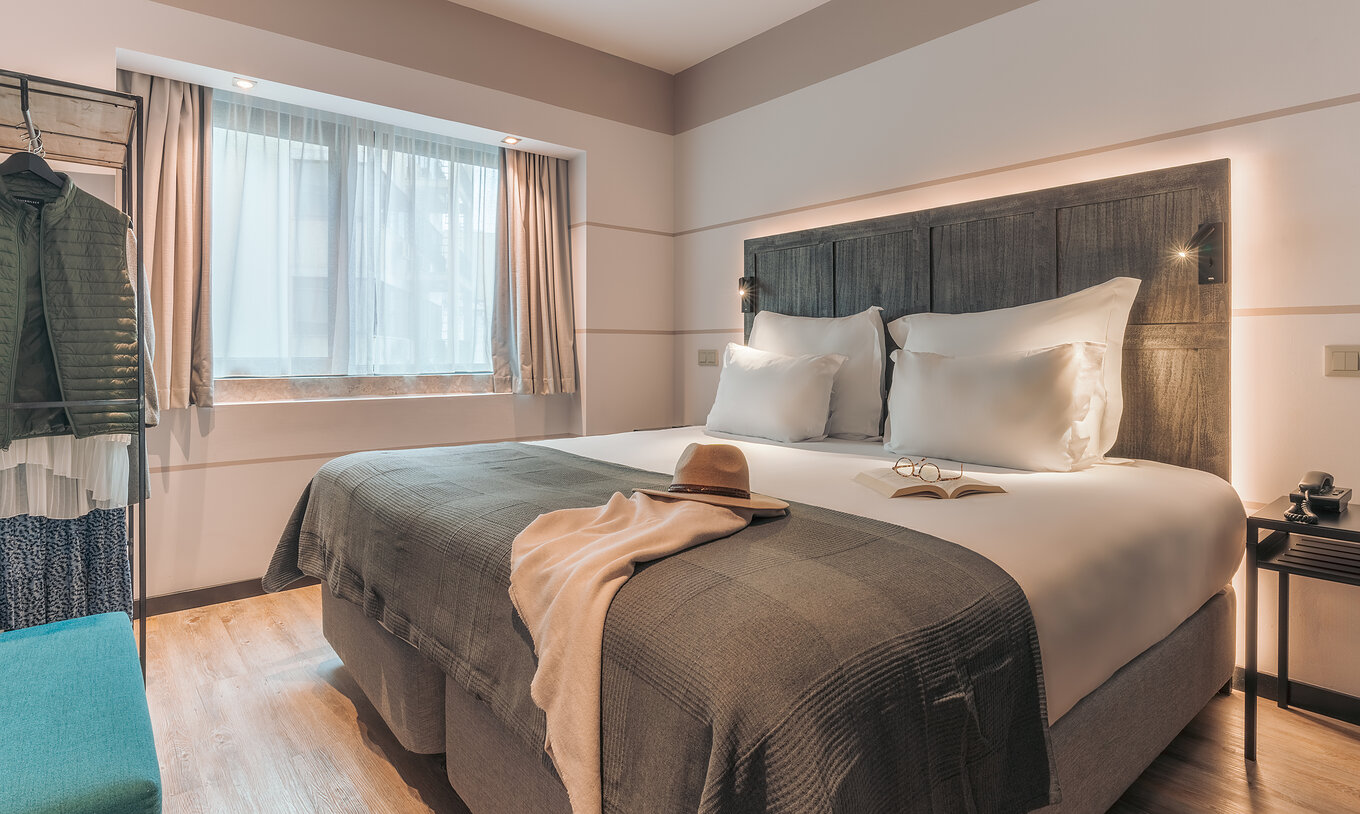 La Junior Suite del Pestana Lisboa Vintage tiene una cama matrimonial con una manta, un sofá azul, mesa de noche y un armario