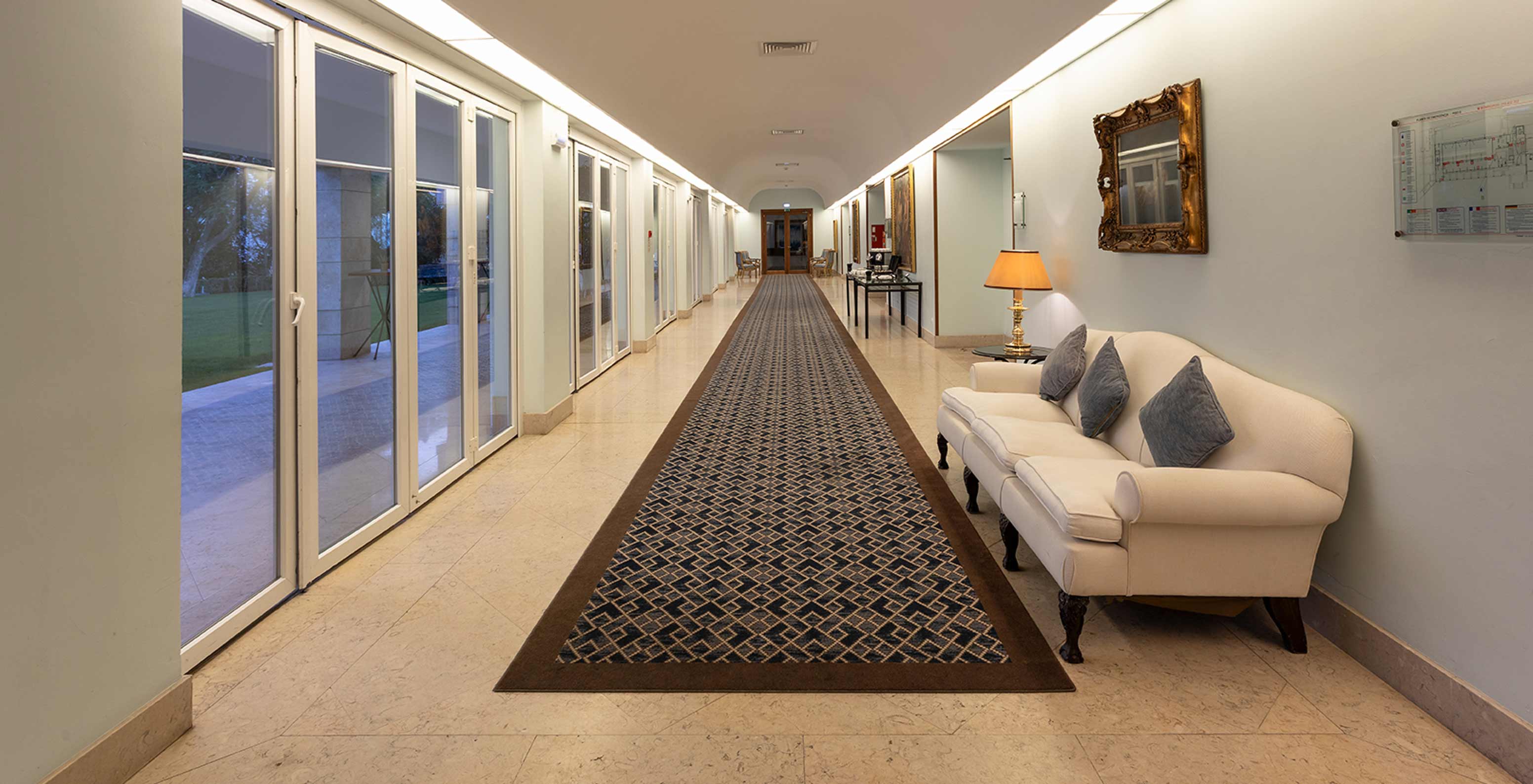 El Pestana Palace Lisboa tiene un foyer con alfombra azul larga, sofá y grandes ventanas con cortinas largas