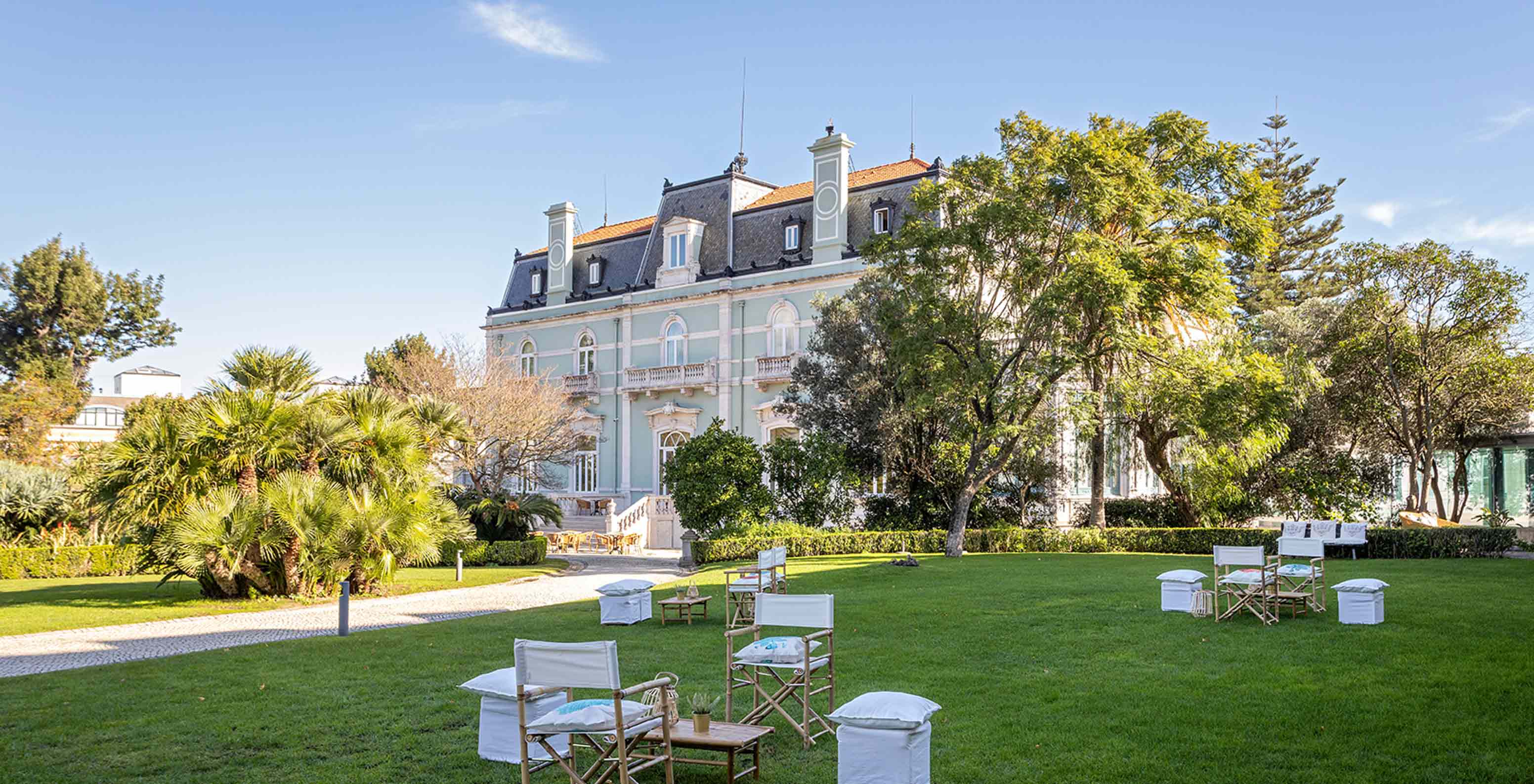 El Pestana Palace Lisboa tiene un jardín con mesas y sillas sobre césped verde, cerca del edificio principal