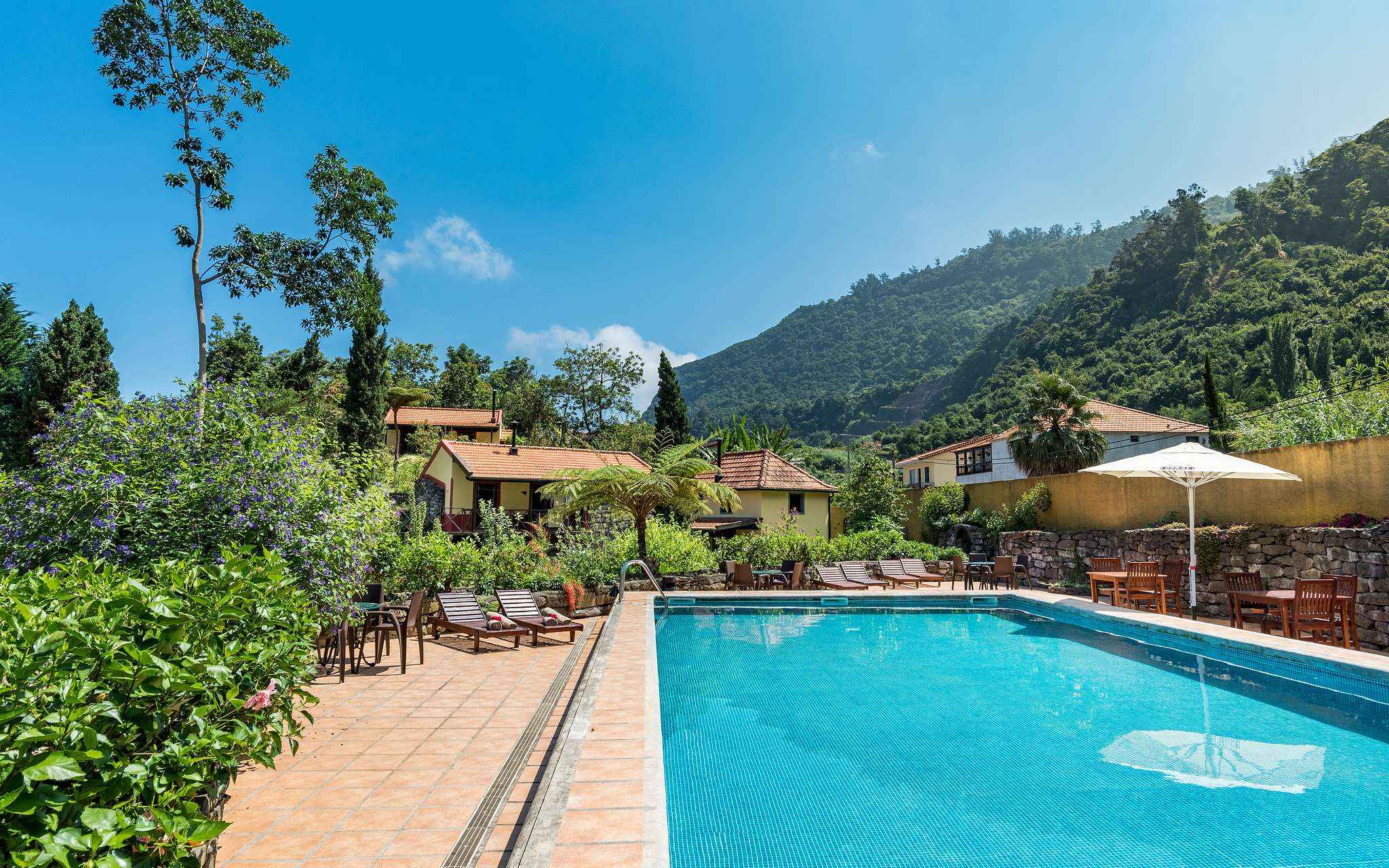 Piscina de Pestana Quinta do Arco, hotel de turismo rural en Madeira, con tumbonas, vegetación, villas y montañas