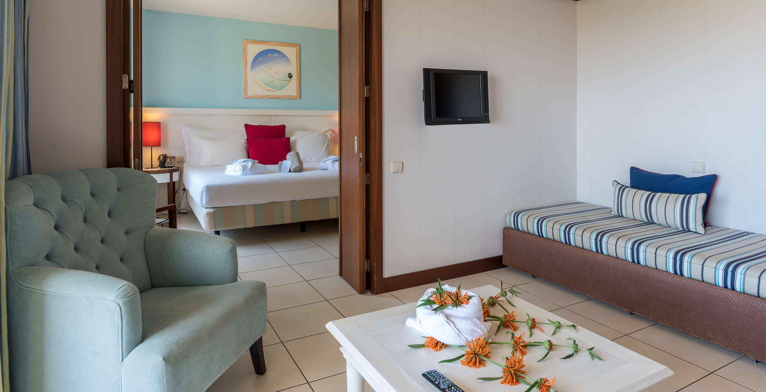 La Suite Apartamento T1 del Pestana Porto Santo All Inclusive tiene un cuarto con cama y una sala con sofá y televisión