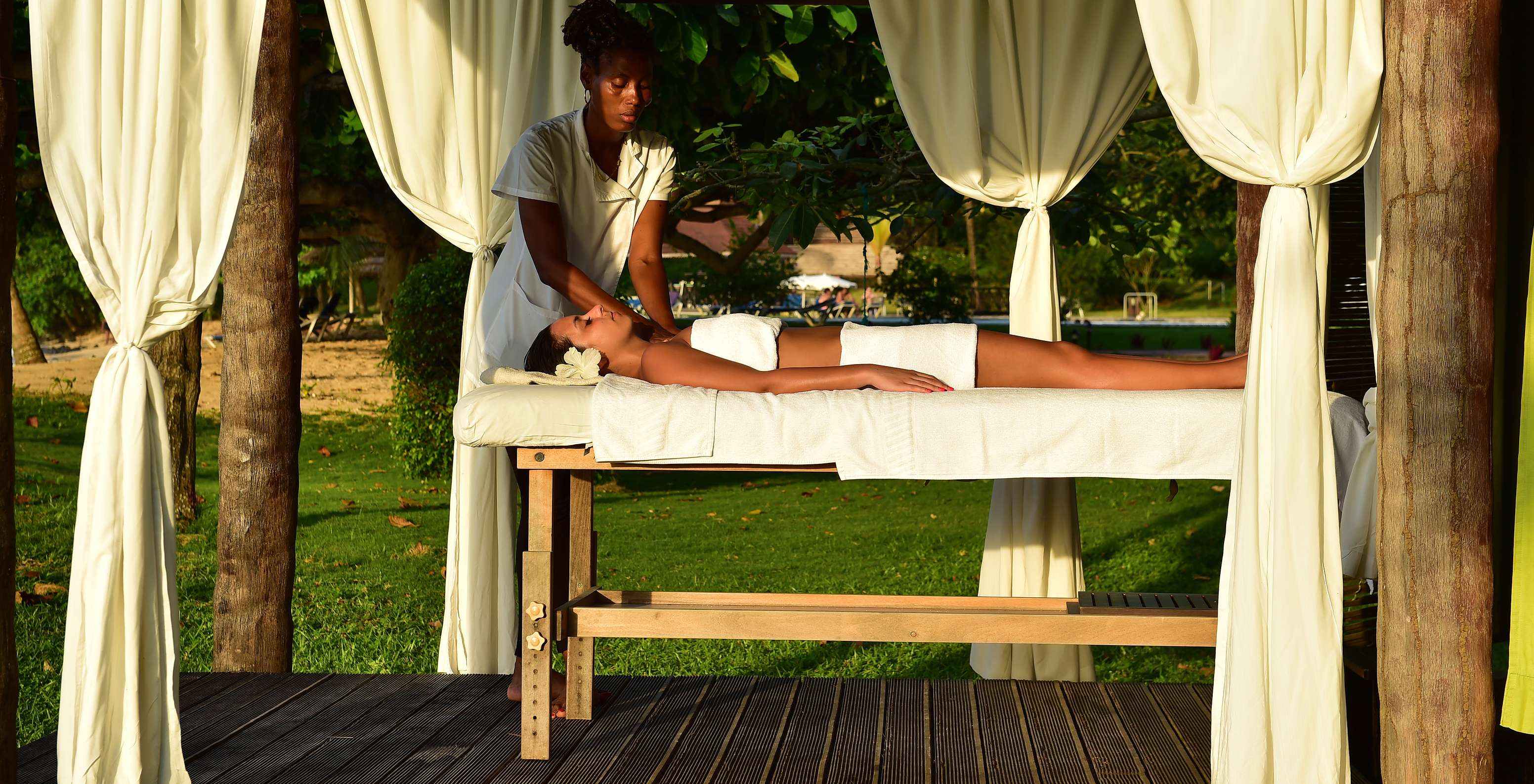 Chica con flor en el cabello recibe masaje al aire libre en el hotel para vacaciones con piscina y spa frente a la playa
