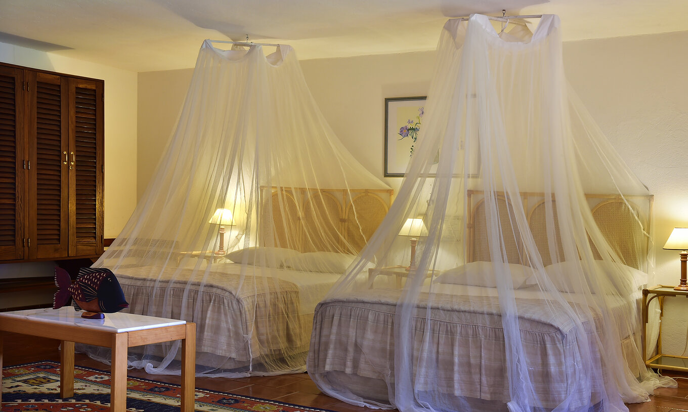 La Junior Suite del Pestana Miramar São Tomé tiene dos camas matrimoniales con mosquitero y tres mesas de noche