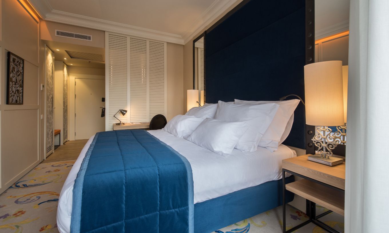La Habitación Superior Plus del Pestana Plaza Mayor Madrid tiene una cama doble con una colcha azul y una alfombra.