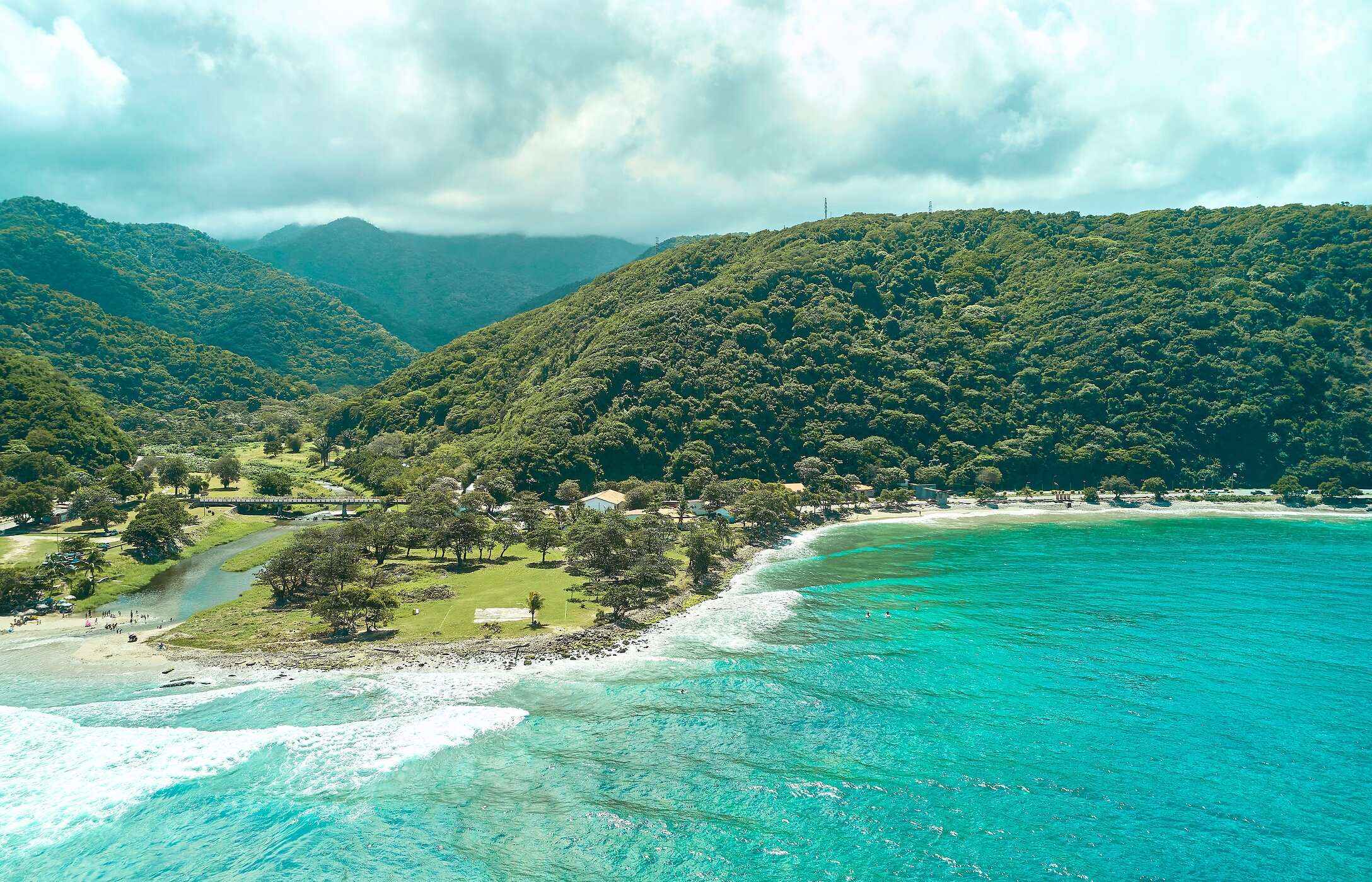 Vista aérea de la playa de La Punta en Venezuela, con aguas cristalinas, rodeada de montañas verdes.