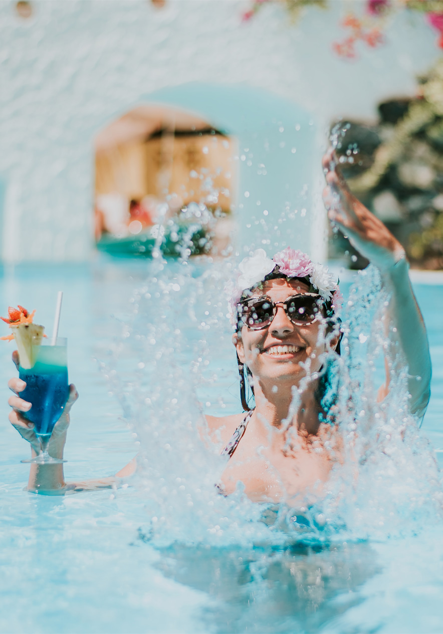 Mujer feliz jugando con el agua, con un cóctel en la mano, disfrutando del paquete todo incluido sin preocupaciones