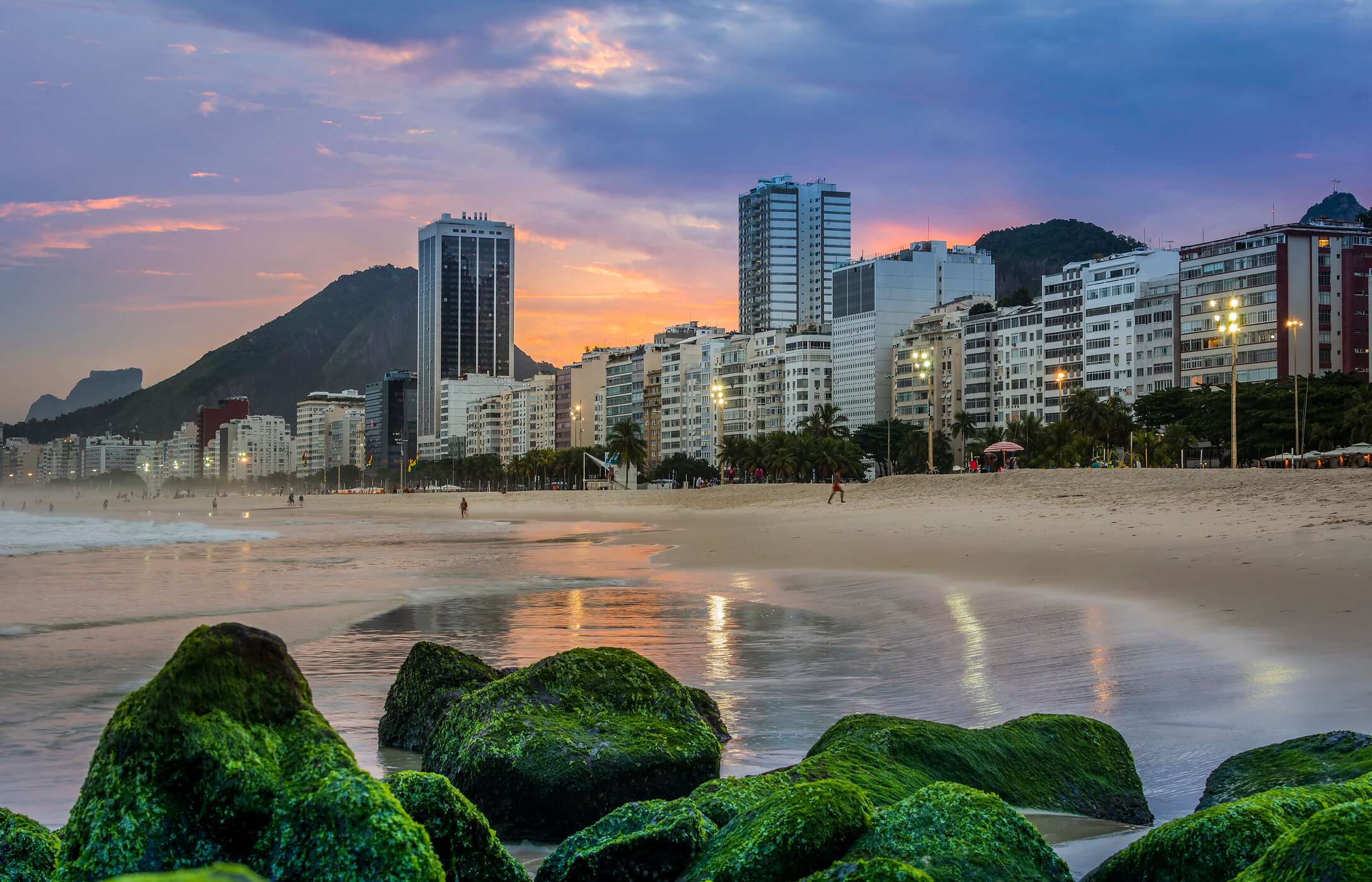 Copacabana-strand, met goudkleurig zand, zeegolven en een drukke promenade, omgeven door gebouwen en bergen op de achtergrond
