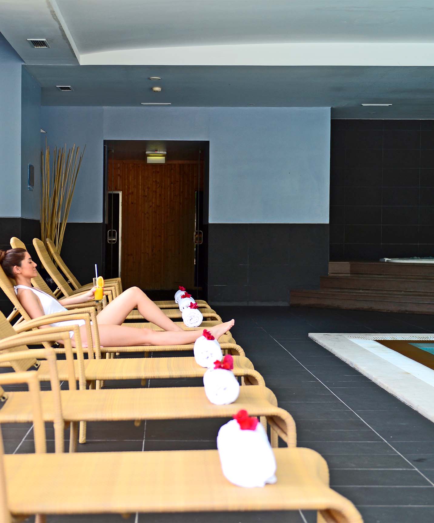 Binnenzwembad met metalen trap, jacuzzi, ligbedden met handdoeken en een liggende dame