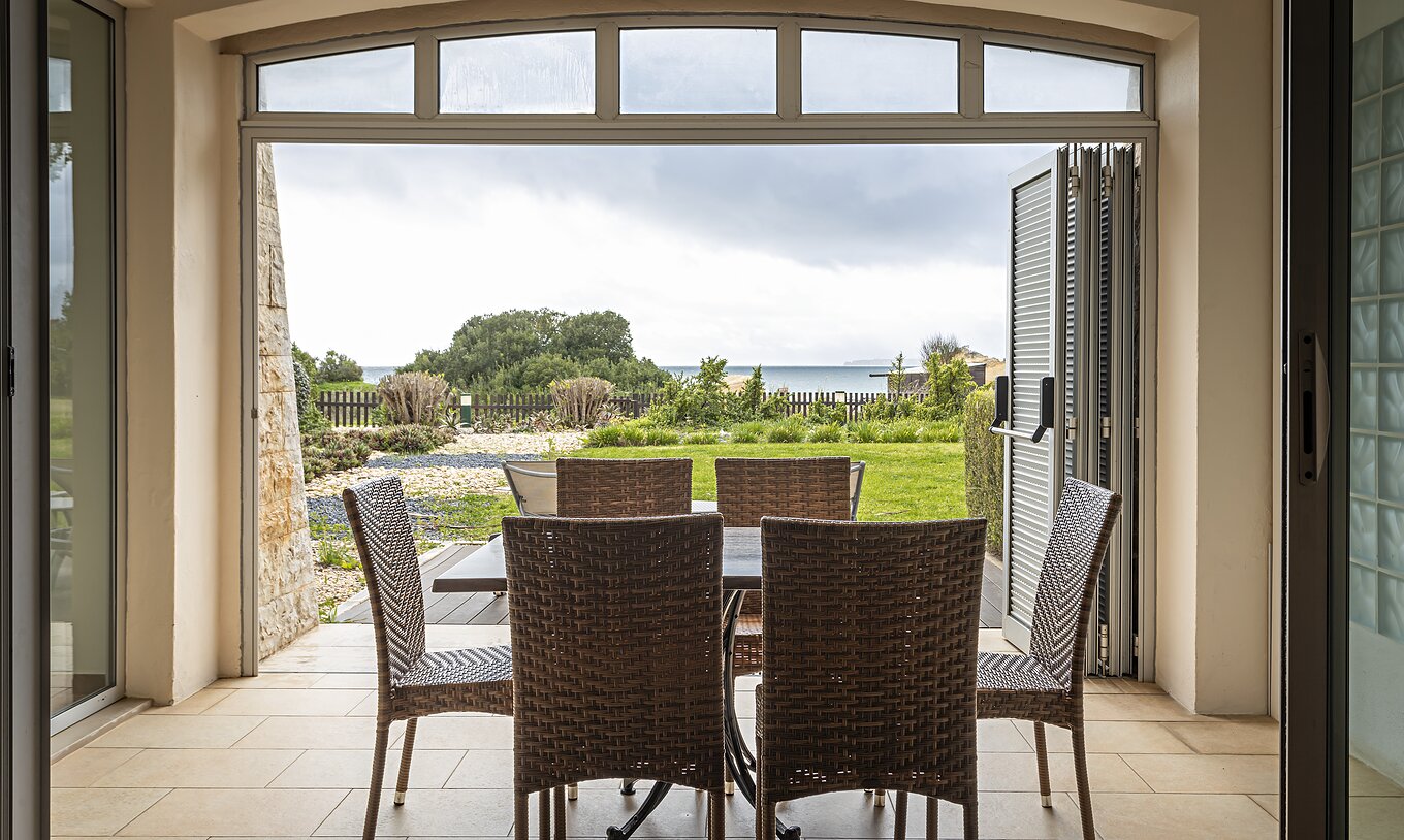 De Cliff Suite T2 in Pestana Alvor Praia heeft een veranda met een tafel en stoelen en een tuin met uitzicht op het strand