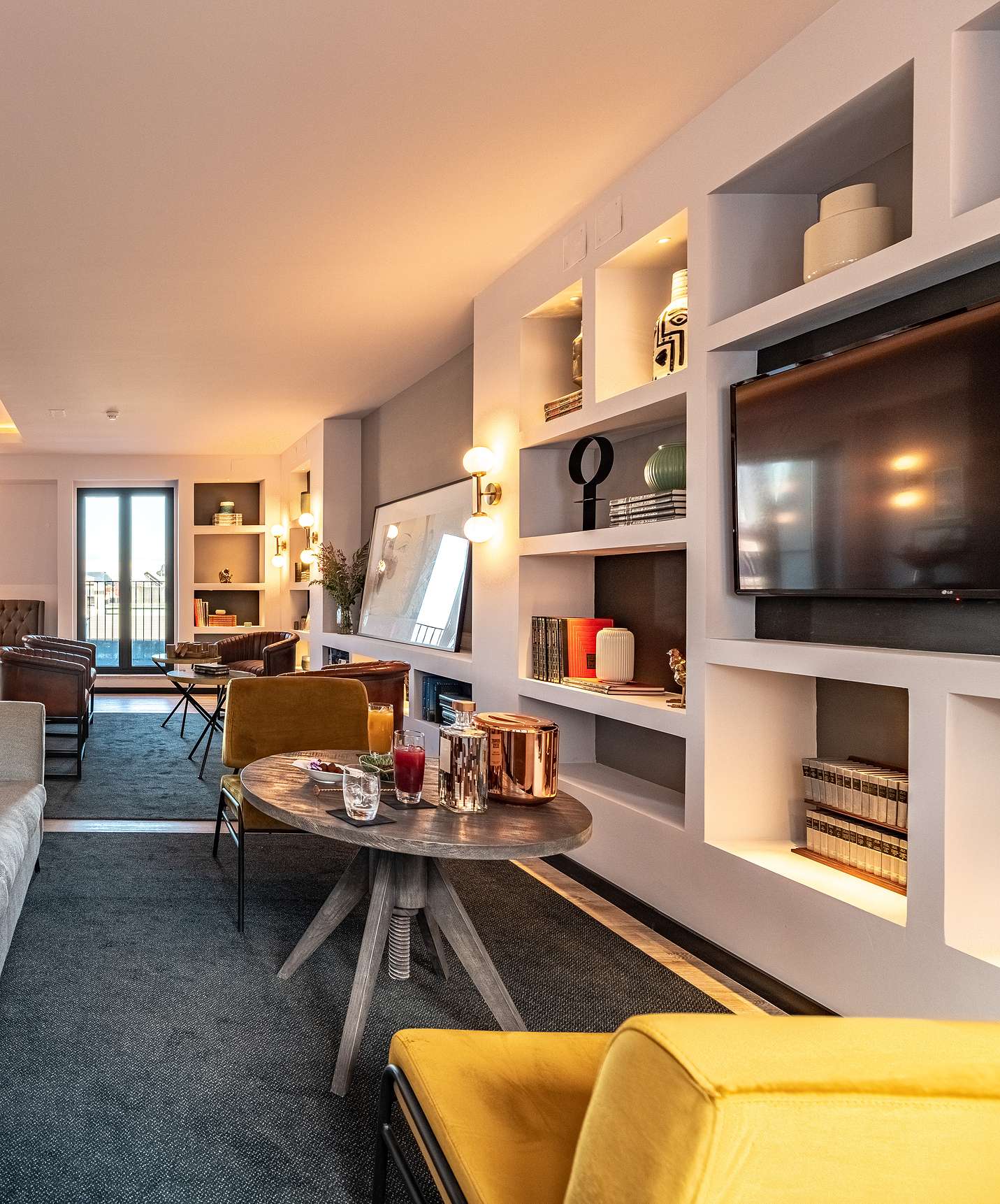 Lounge met banken stoelen tafels schilderijen tv tapijten en decor met ramen met stadszicht