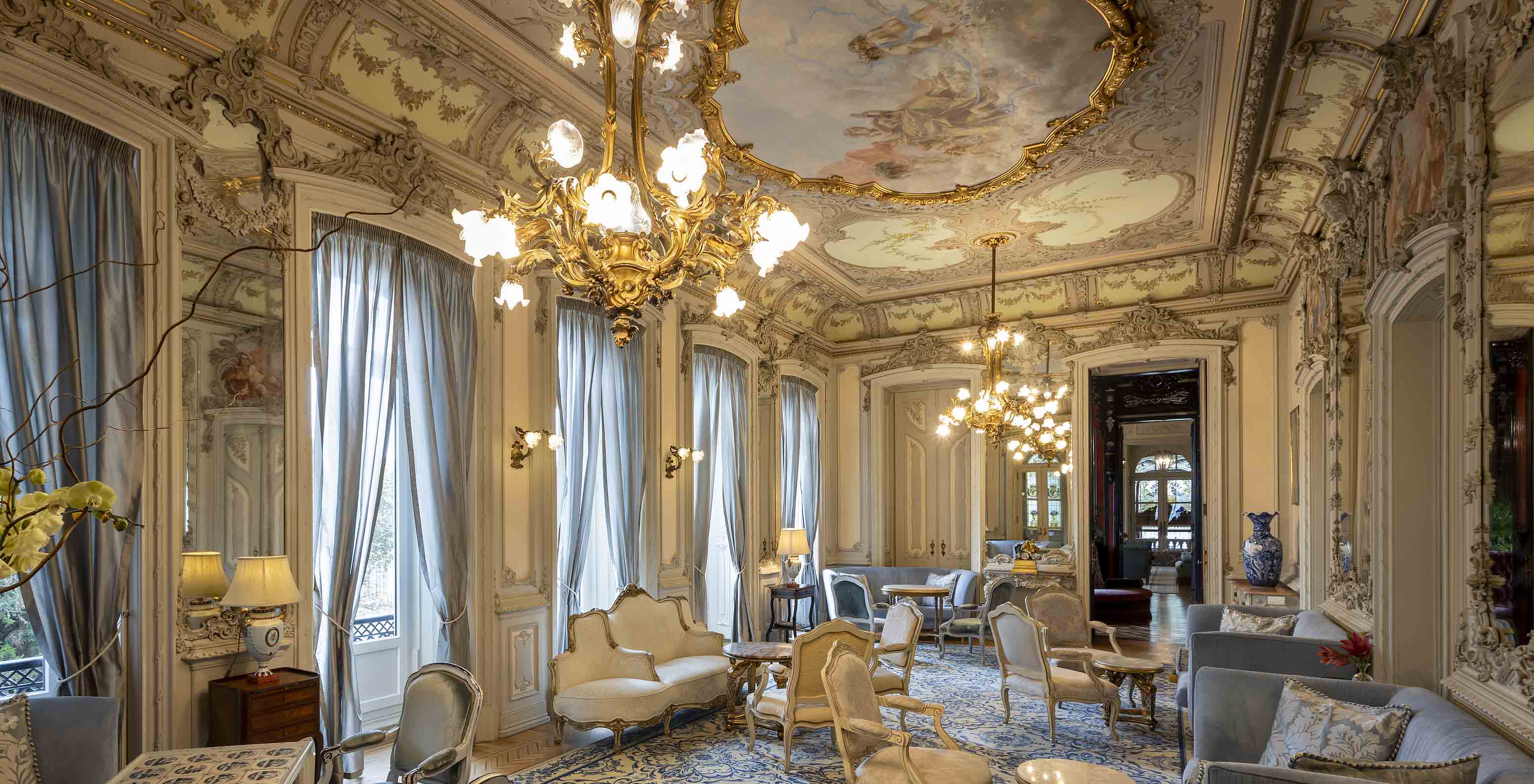 Het Pestana Palace Lisboa heeft een lounge in het paleis met versierde muren en plafond, en blauwe fauteuils en banken