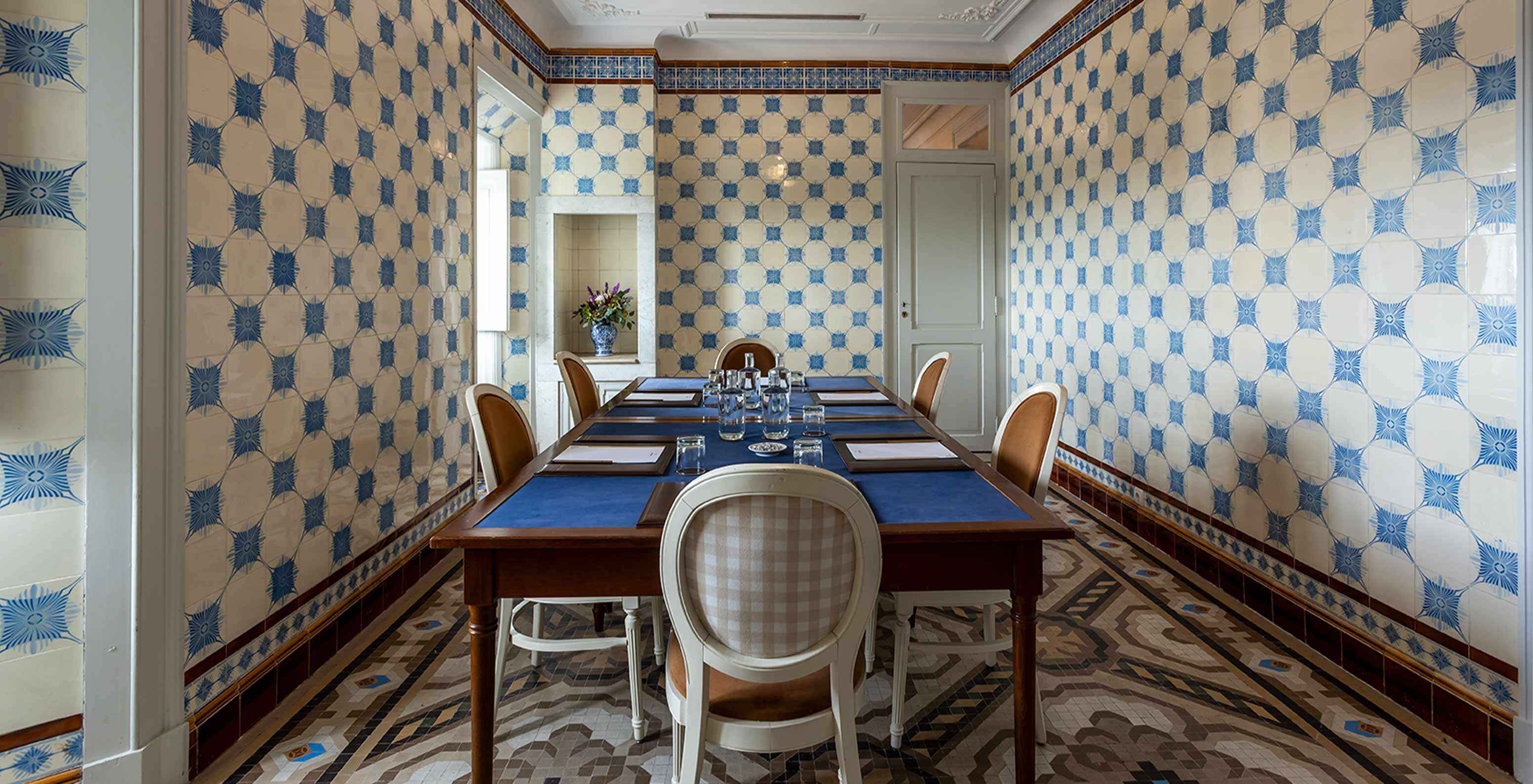 Pestana Palace Lisboa heeft een vergaderzaal met blauwe en witte tegels en een tafel omringd door witte stoelen	