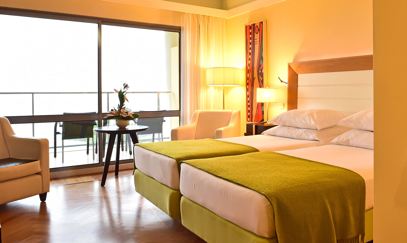 De Superior Kamer van Pestana Promenade heeft twee bedden met een groene dekbed en een groot raam naar het balkon